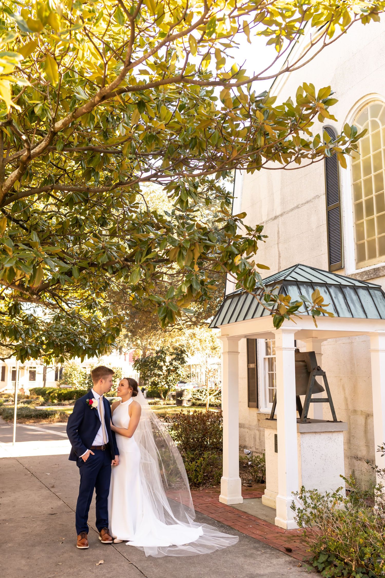 A couple shares a romantic moment outside a church entrance with golden autumn foliage overhead.