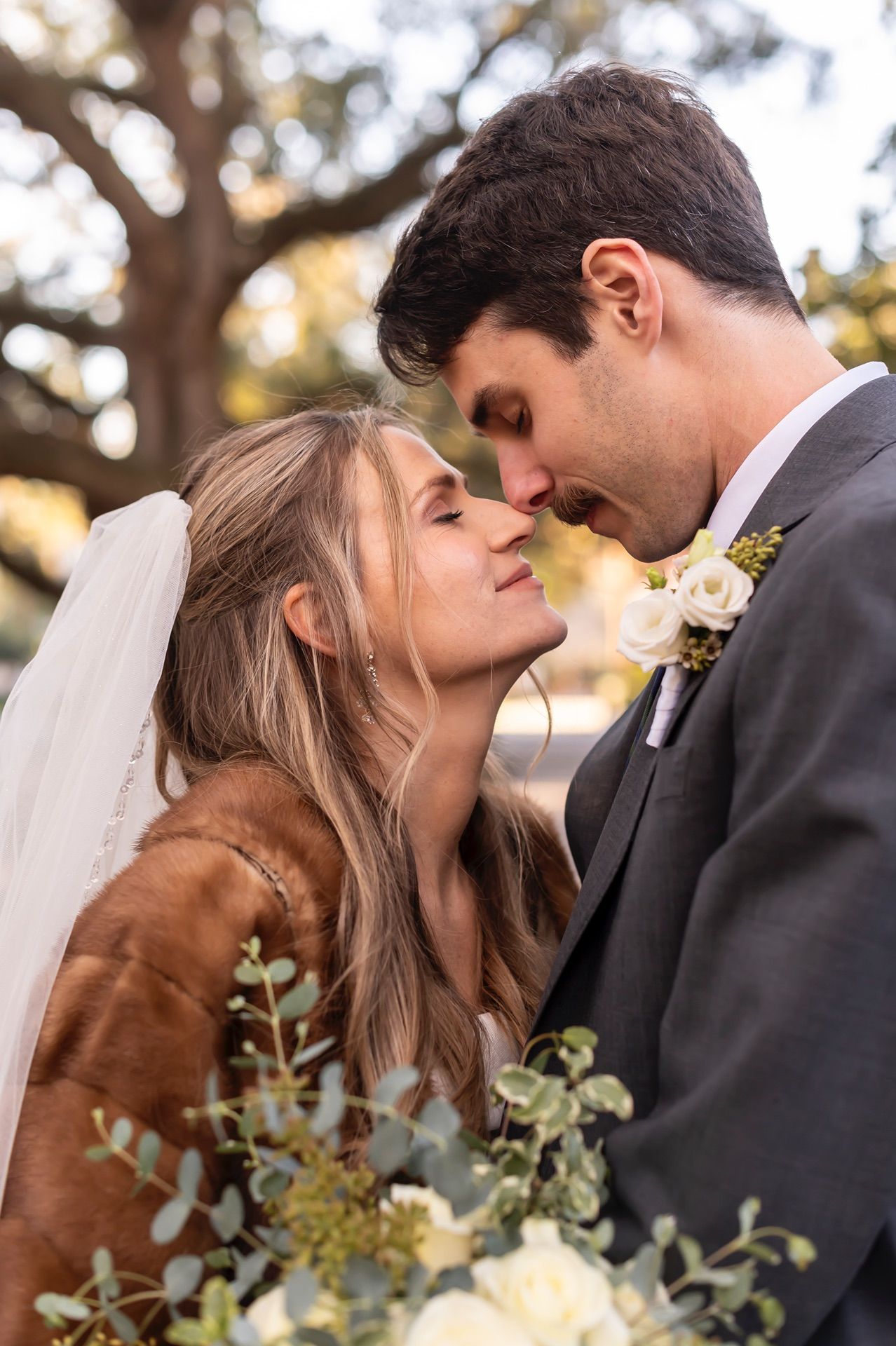 Romantic wedding couple shares tender moments in a series of outdoor portraits with soft golden lighting and greenery.