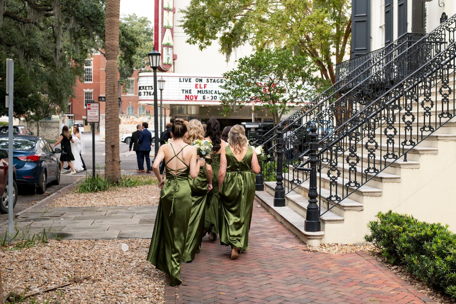 A series of people in graduation robes walking along a brick path next to black metal railings on a sunny day.