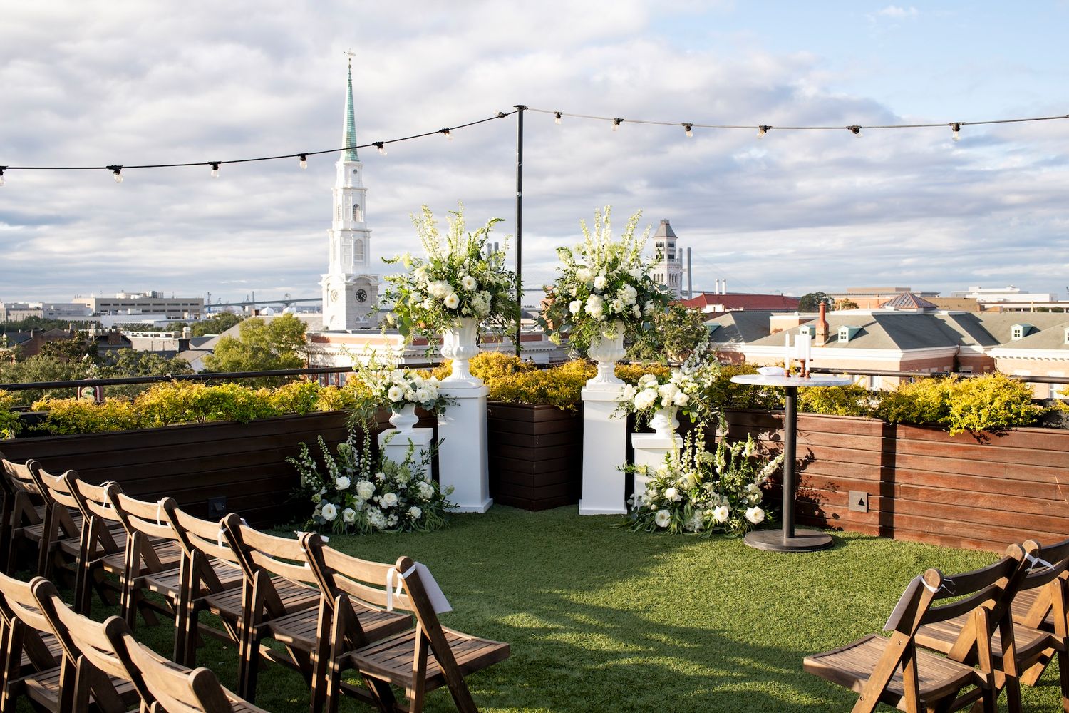 String lights illuminate an outdoor rooftop venue with tables and chairs set up for an evening event.