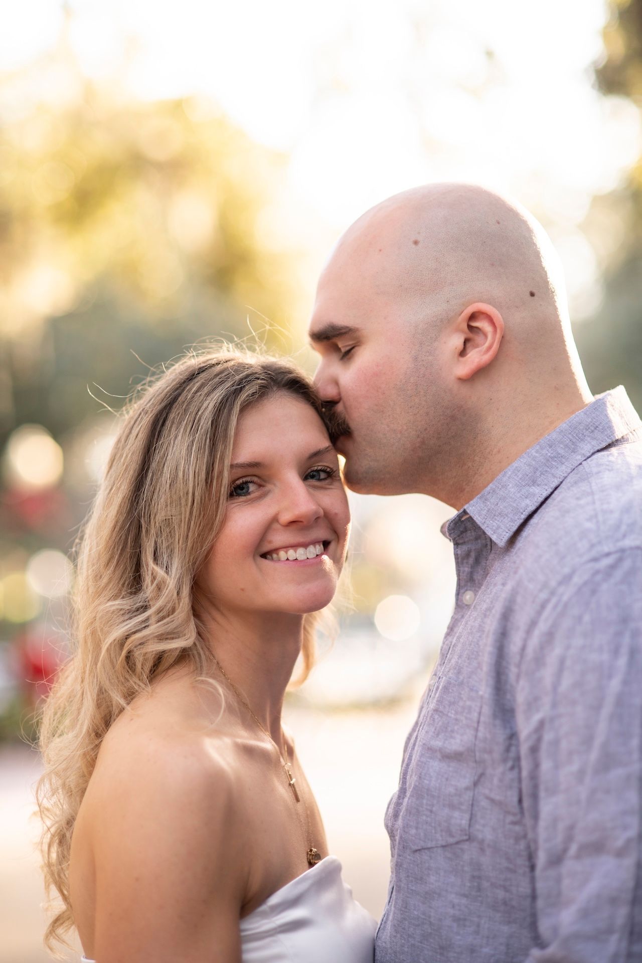 A romantic couple shares a tender moment outdoors during golden hour with soft bokeh lighting in the background.