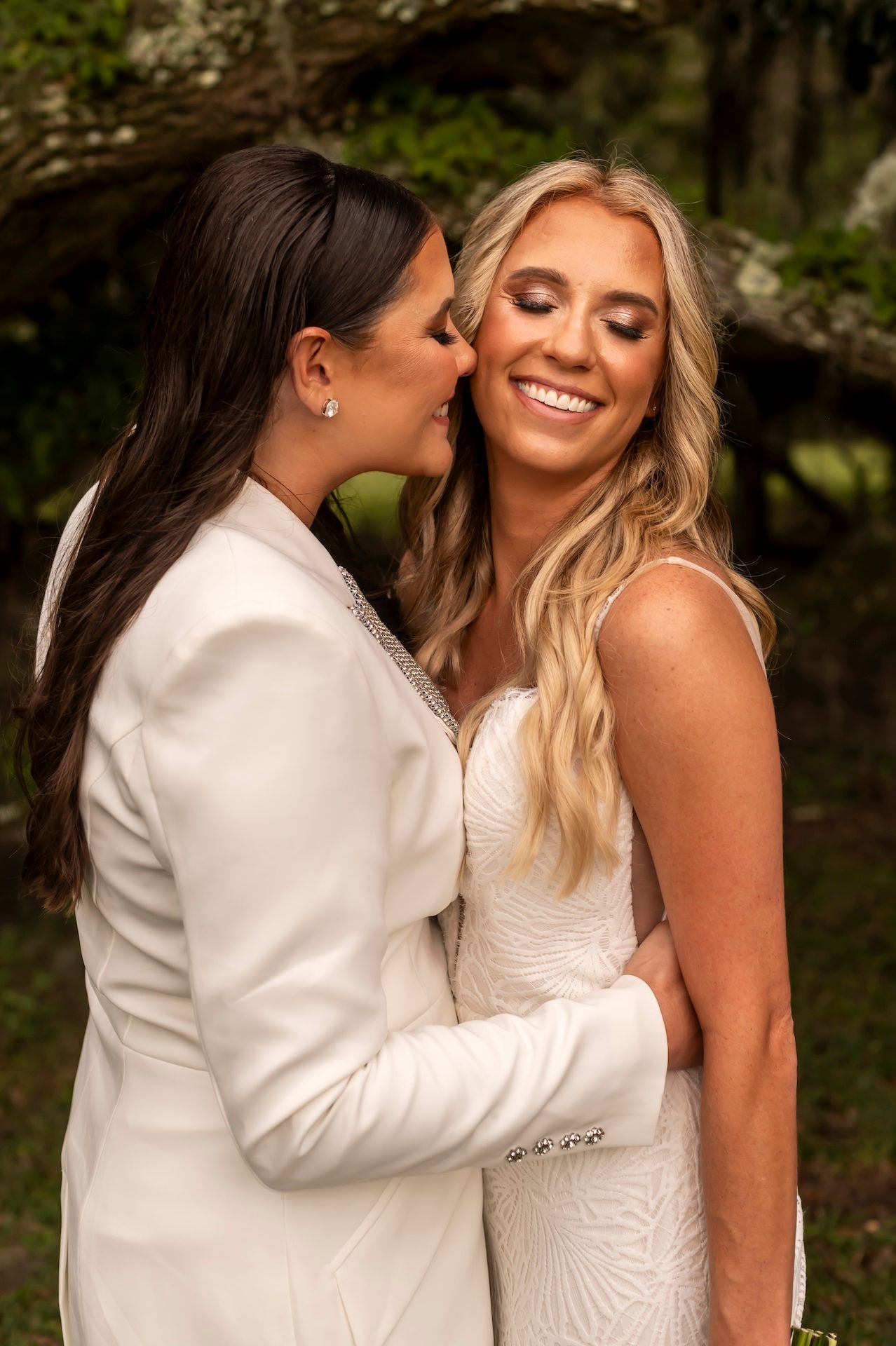 A romantic wedding couple in white embraces and shares intimate moments in a lush outdoor setting.