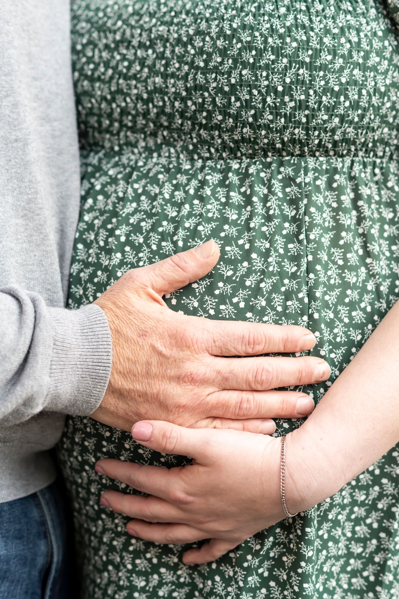 Close up of hands tenderly placed on a pregnant belly covered in a green floral dress.