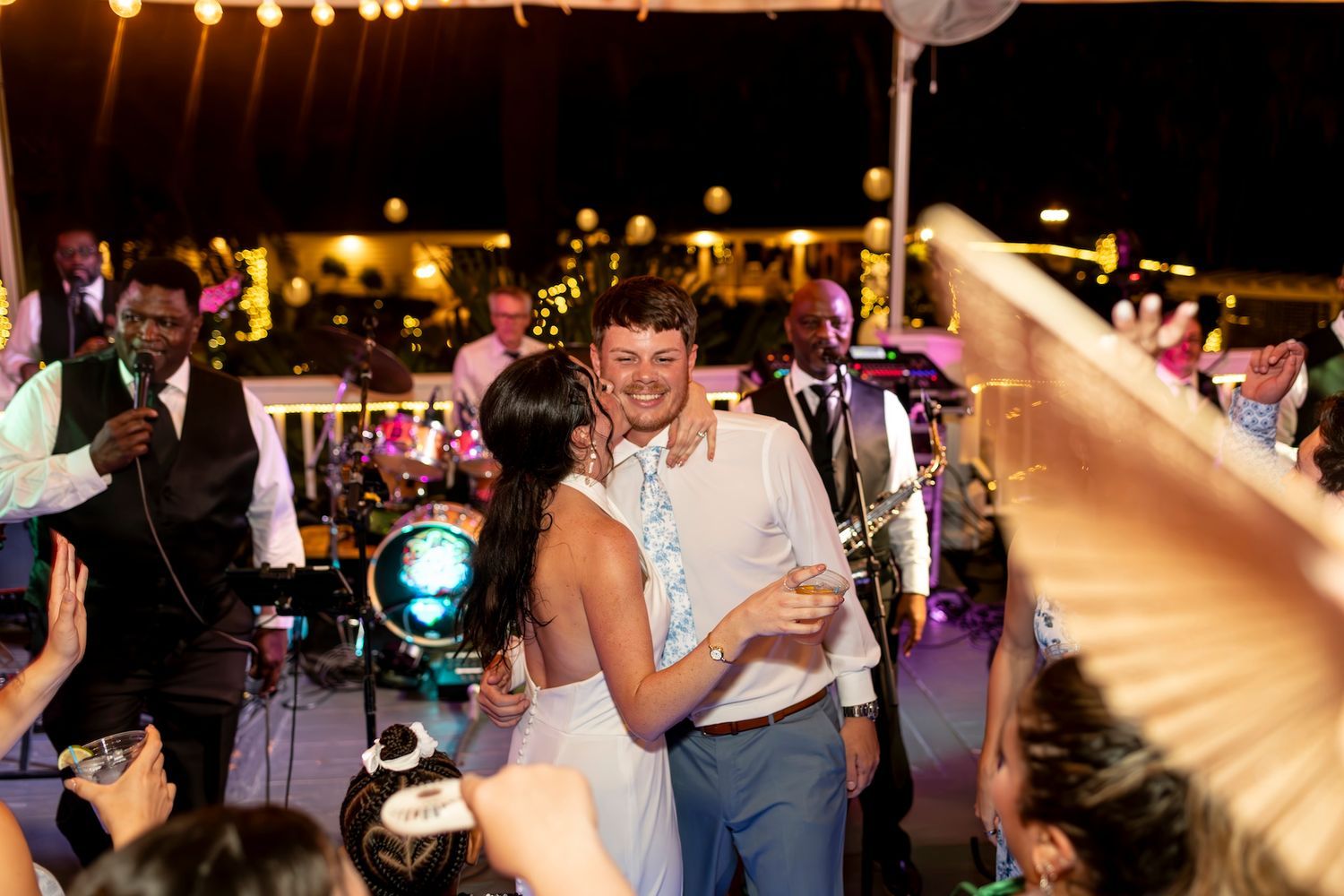 A couple shares a dance together at a nighttime outdoor wedding reception with string lights overhead.
