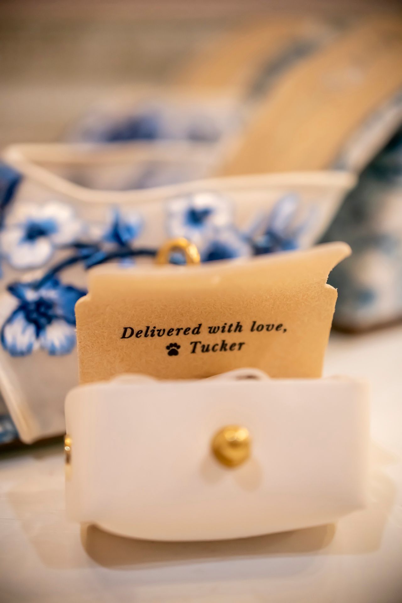 A decorative note card reading 'Delivered with love, Tucker' displayed against blue and white floral background.