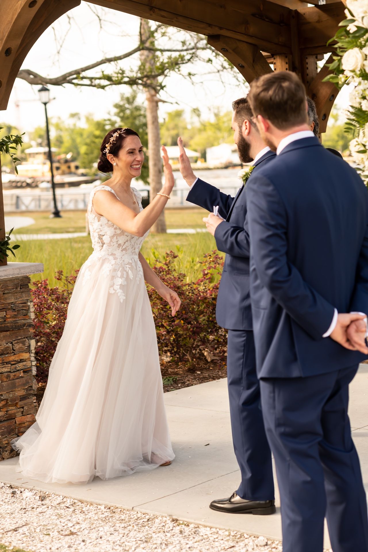 Bride and groom share an energetic high five during their wedding ceremony under a rustic wooden arch.