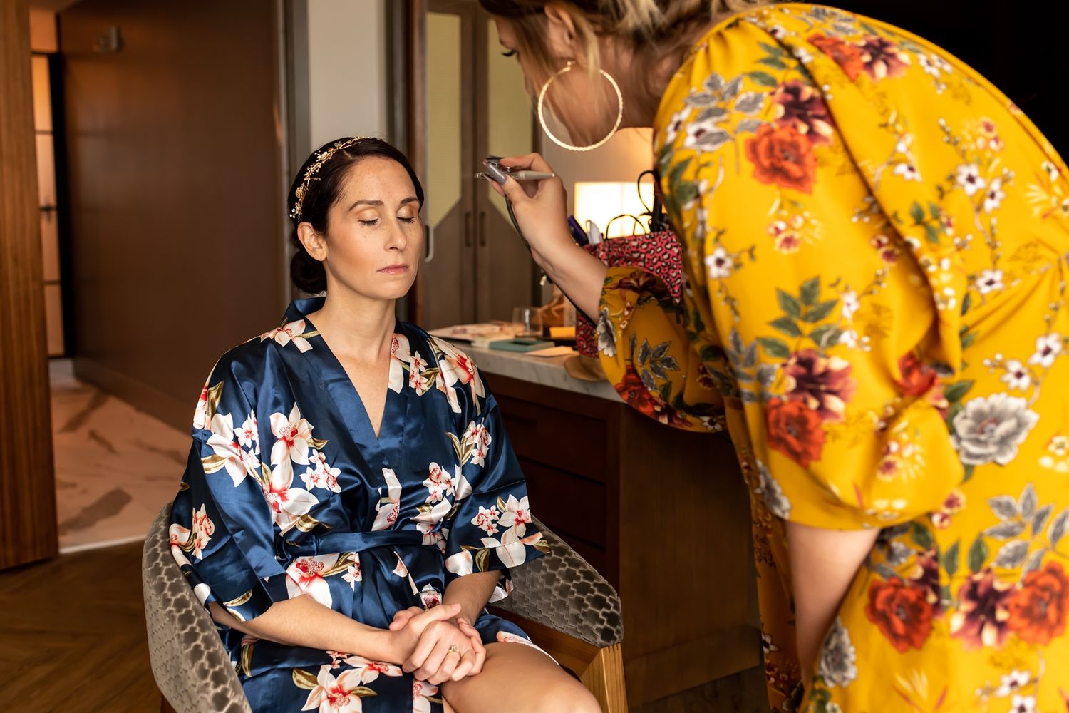 Makeup artist applying cosmetics to a person wearing a blue floral robe during a getting-ready session.