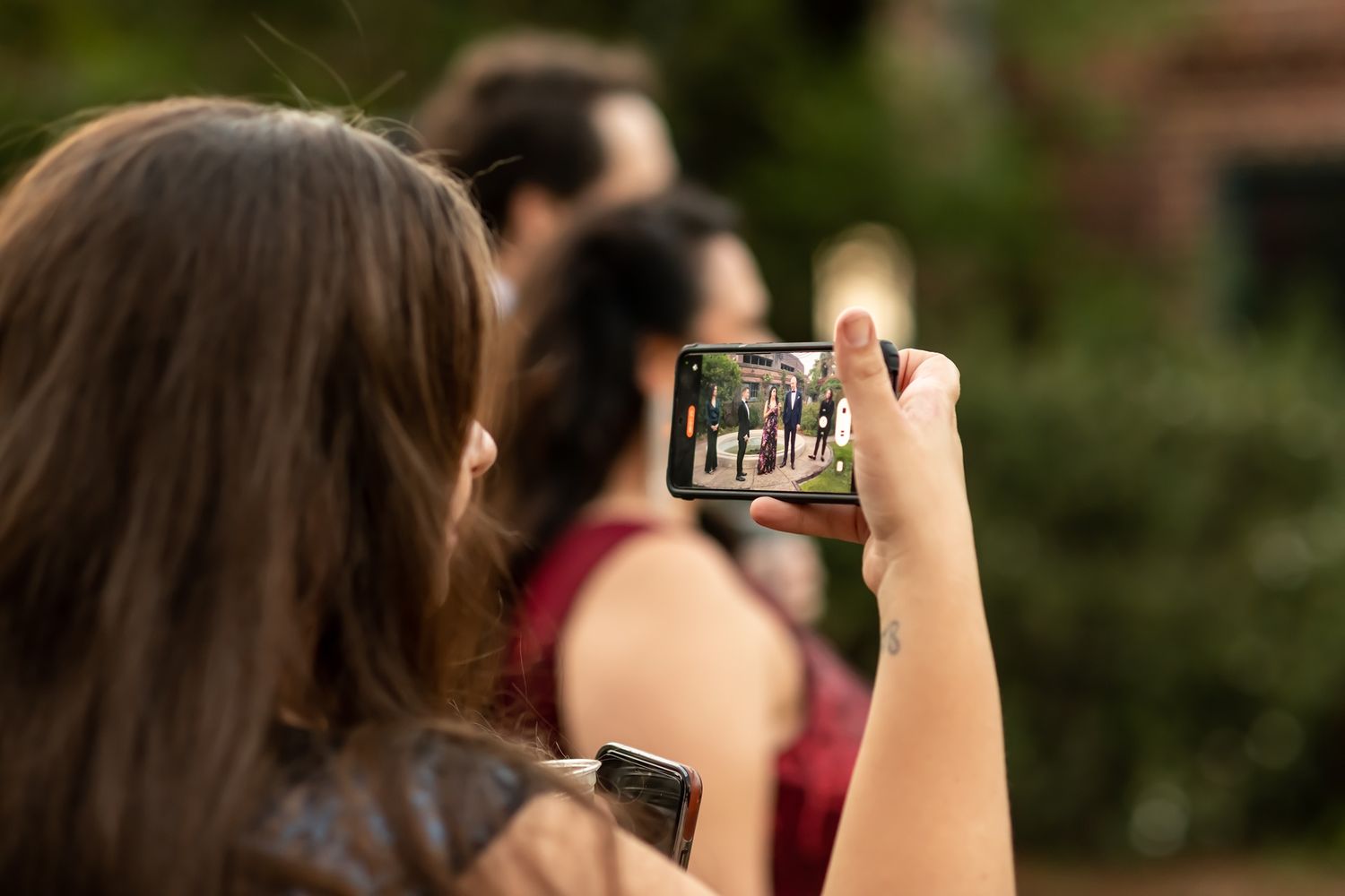 Person holding up smartphone to take photo outdoors with blurred bokeh background.