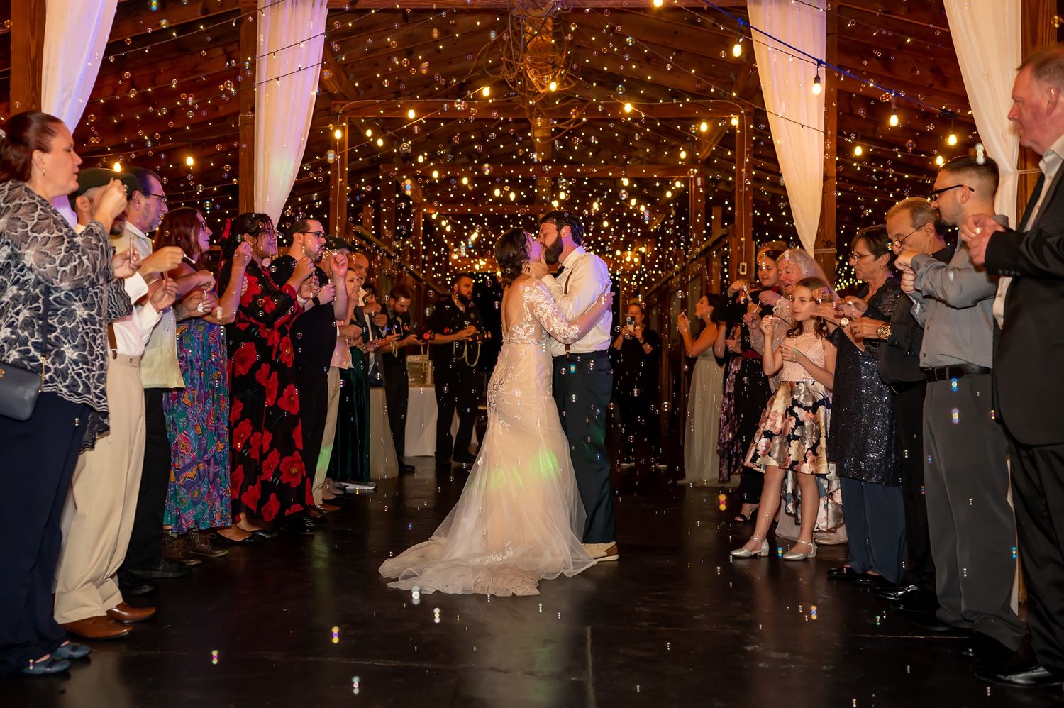 Wedding guests in formal attire line up outdoors at night with sparklers creating a magical send-off tunnel for the newlyweds.