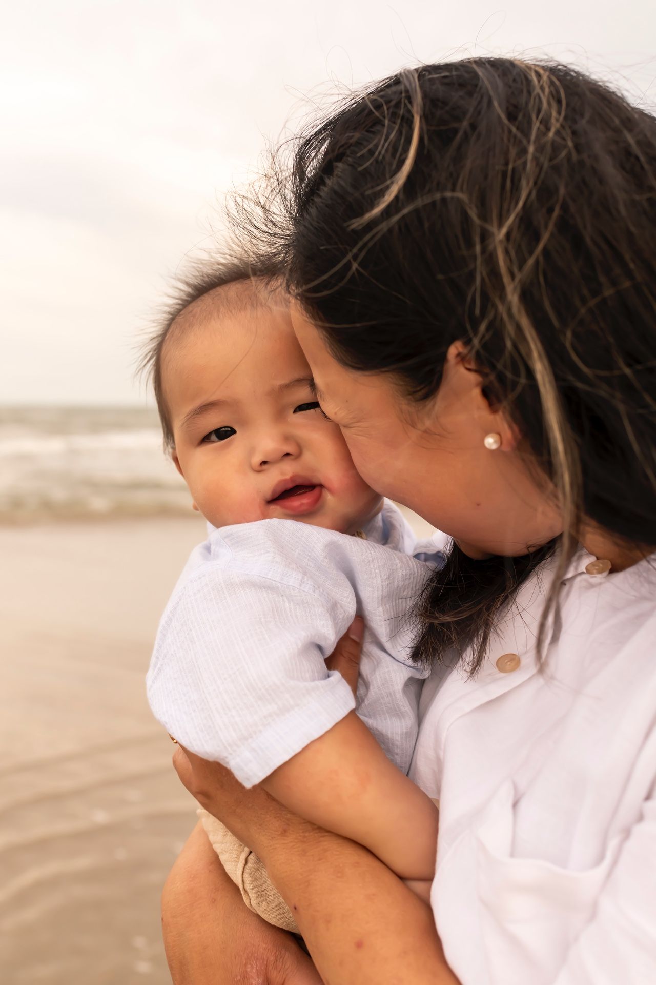 A tender moment between parent and baby sharing joyful laughter together on a peaceful beach at sunset.