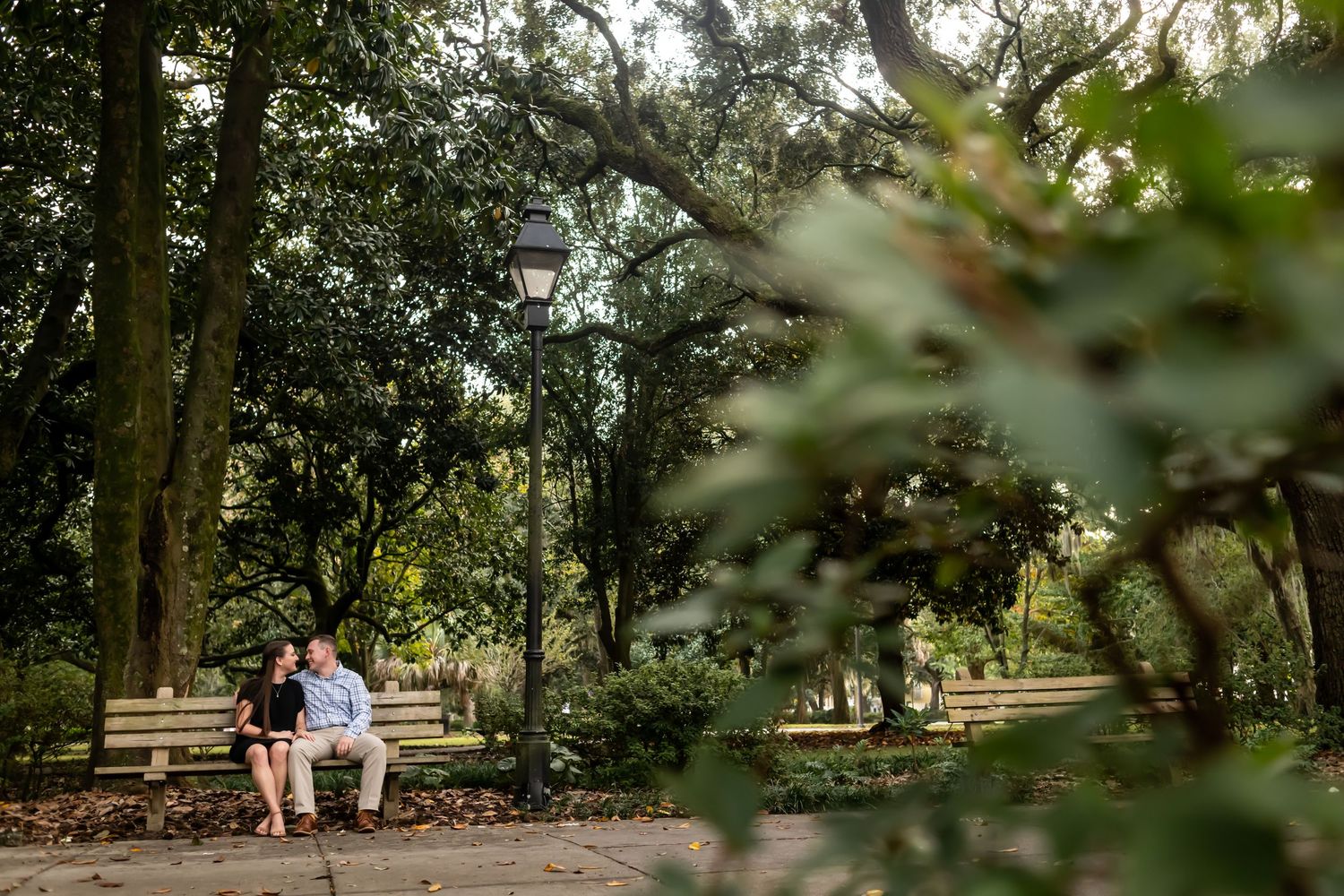 A couple stands among lush trees in a garden setting during a romantic outdoor photo session at golden hour.