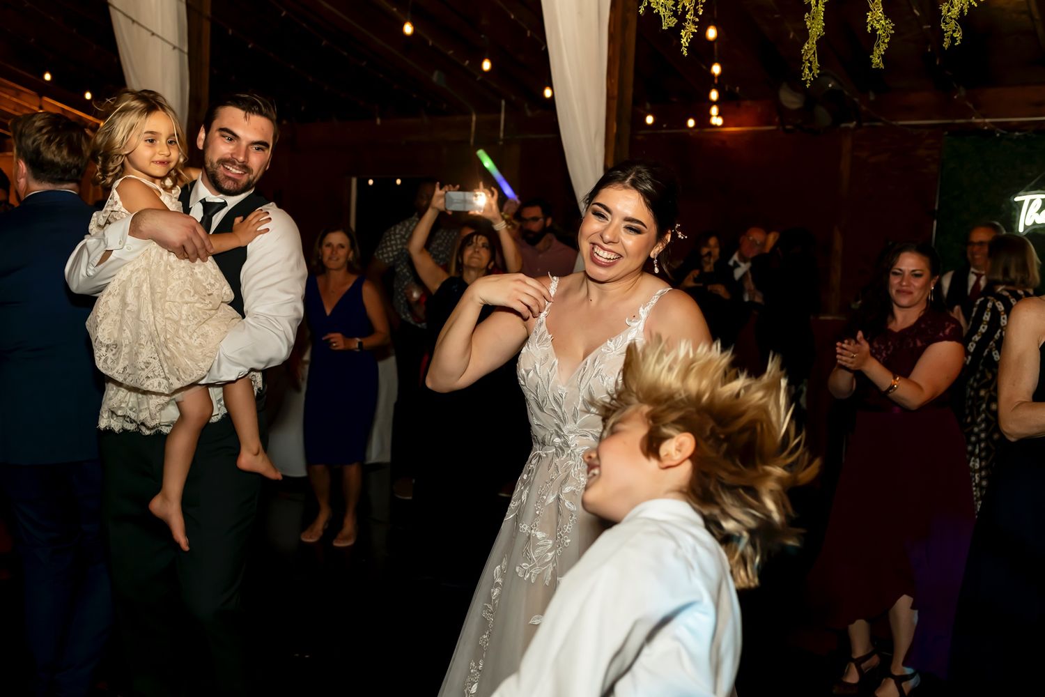 Guests dancing and celebrating energetically at a festive evening wedding reception with beautiful lighting and decor.