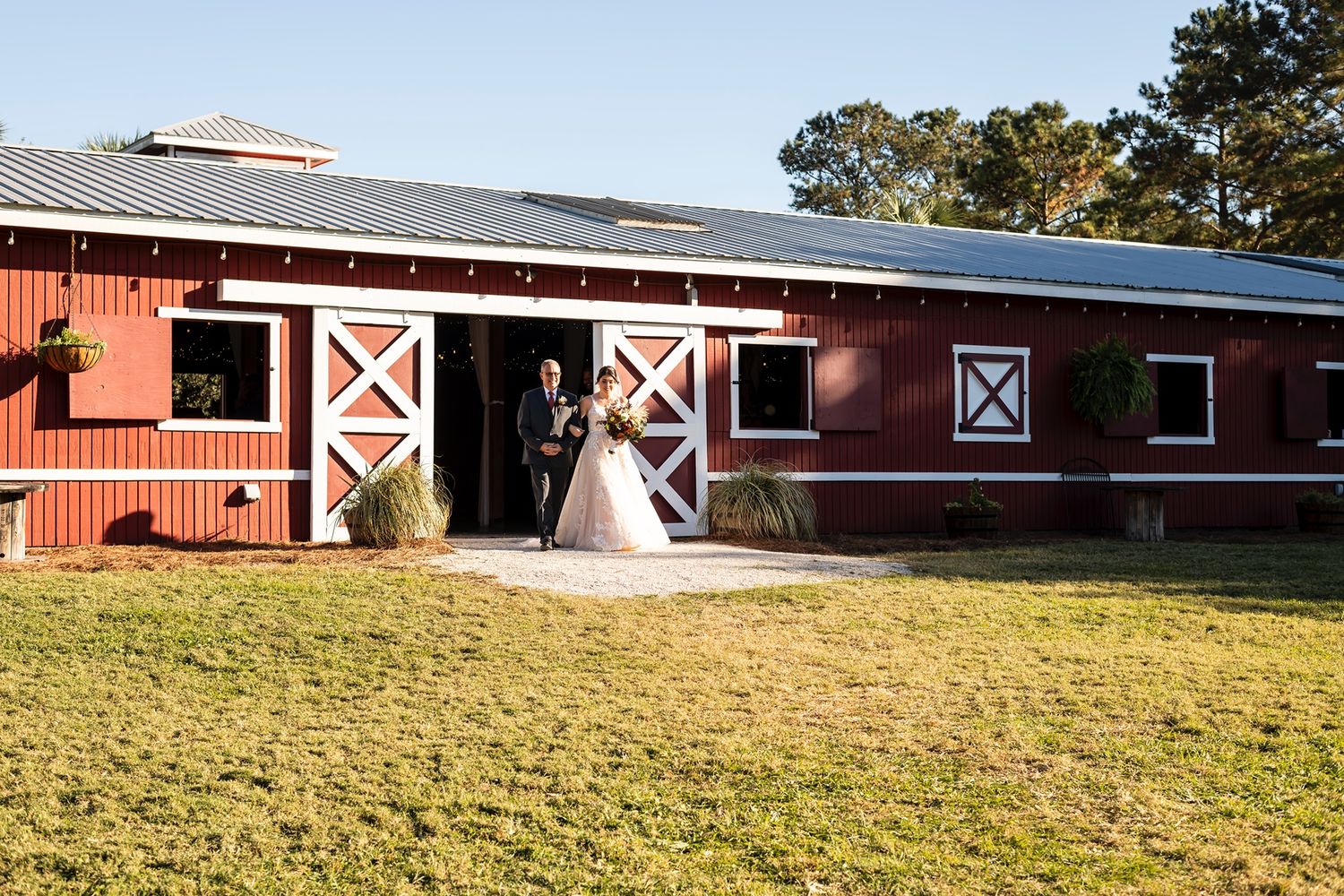 A rustic red barn wedding venue with white trim and large entrance doors on a sunny day with green grass.
