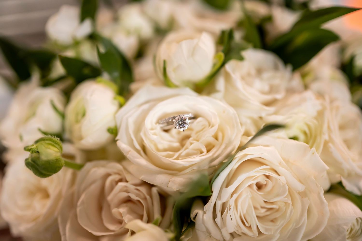 A diamond engagement ring nestles among delicate white garden roses in a romantic bridal bouquet.