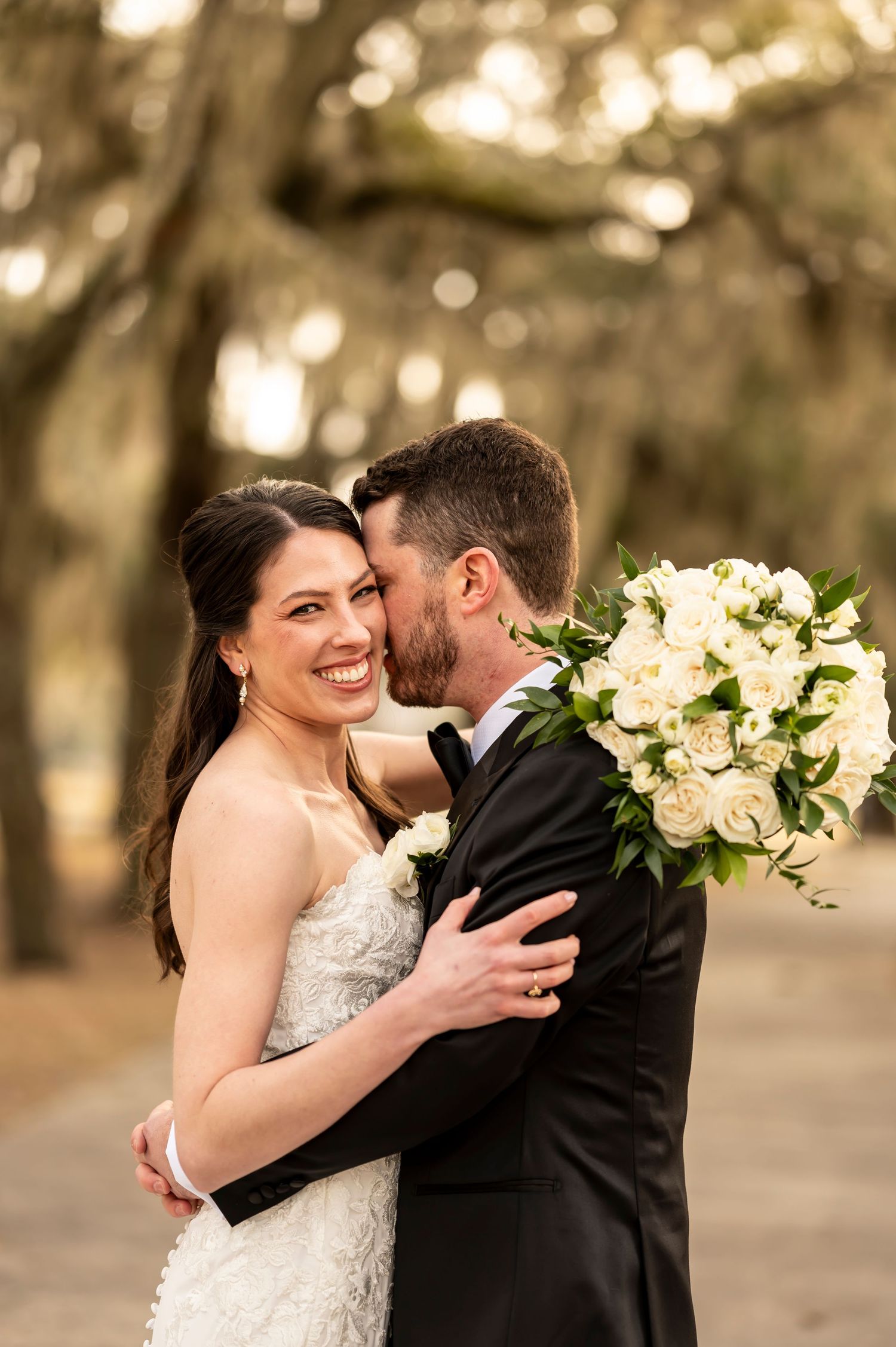 A newlywed couple shares intimate romantic moments during their outdoor wedding photoshoot in a sunlit garden setting.