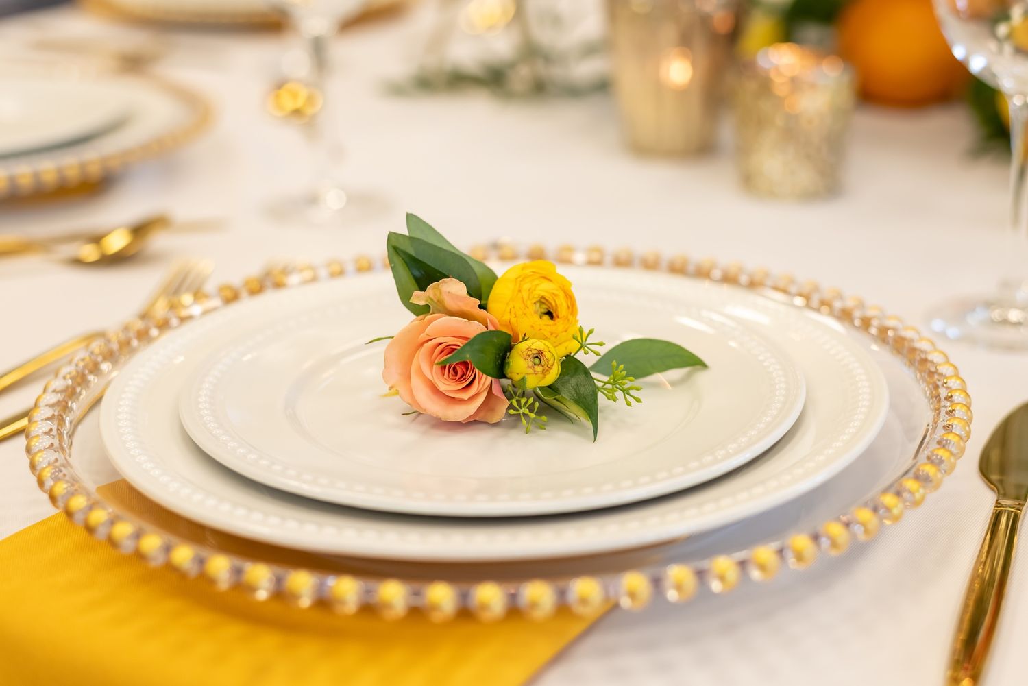 Elegant wedding table settings with gold beaded charger plates and delicate floral centerpieces.