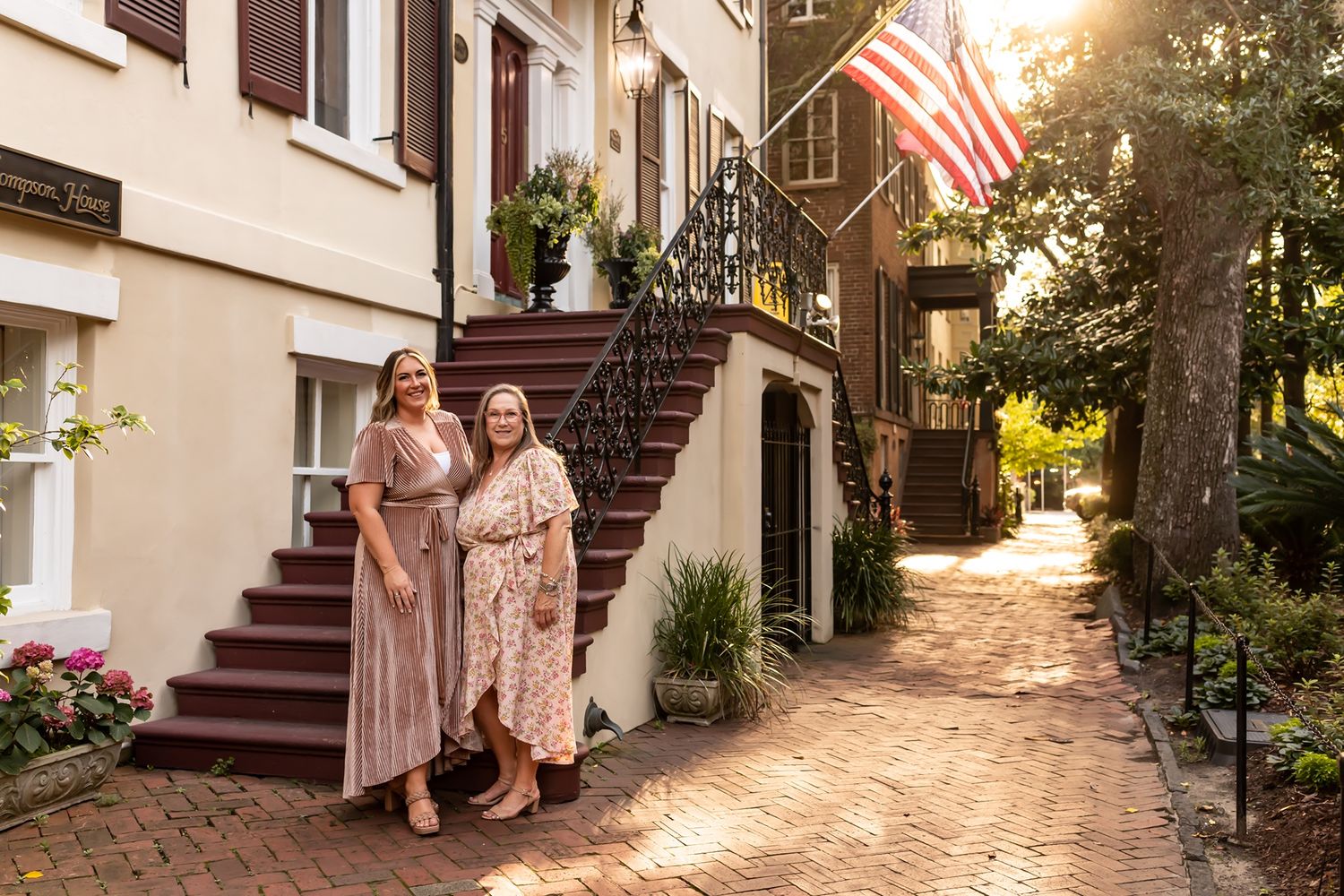 Group stands on a brick staircase in front of a white building with an American flag waving in the background.