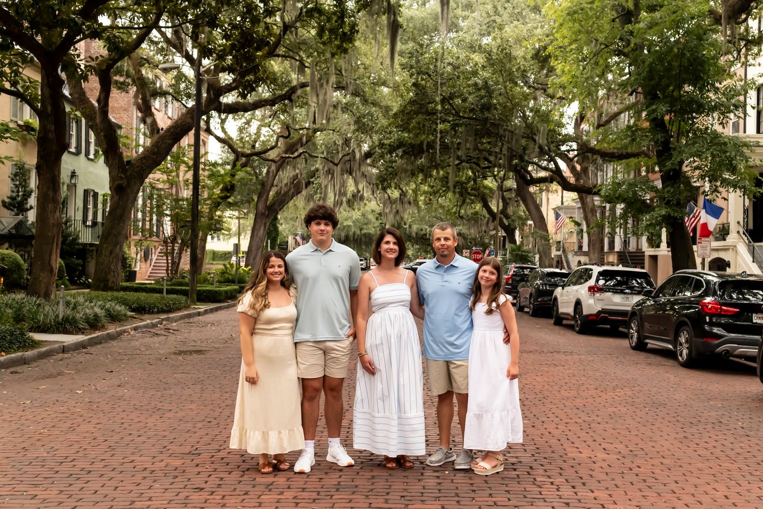 A family group stands together on a brick-paved street with Spanish moss draped trees and historic buildings in the background.