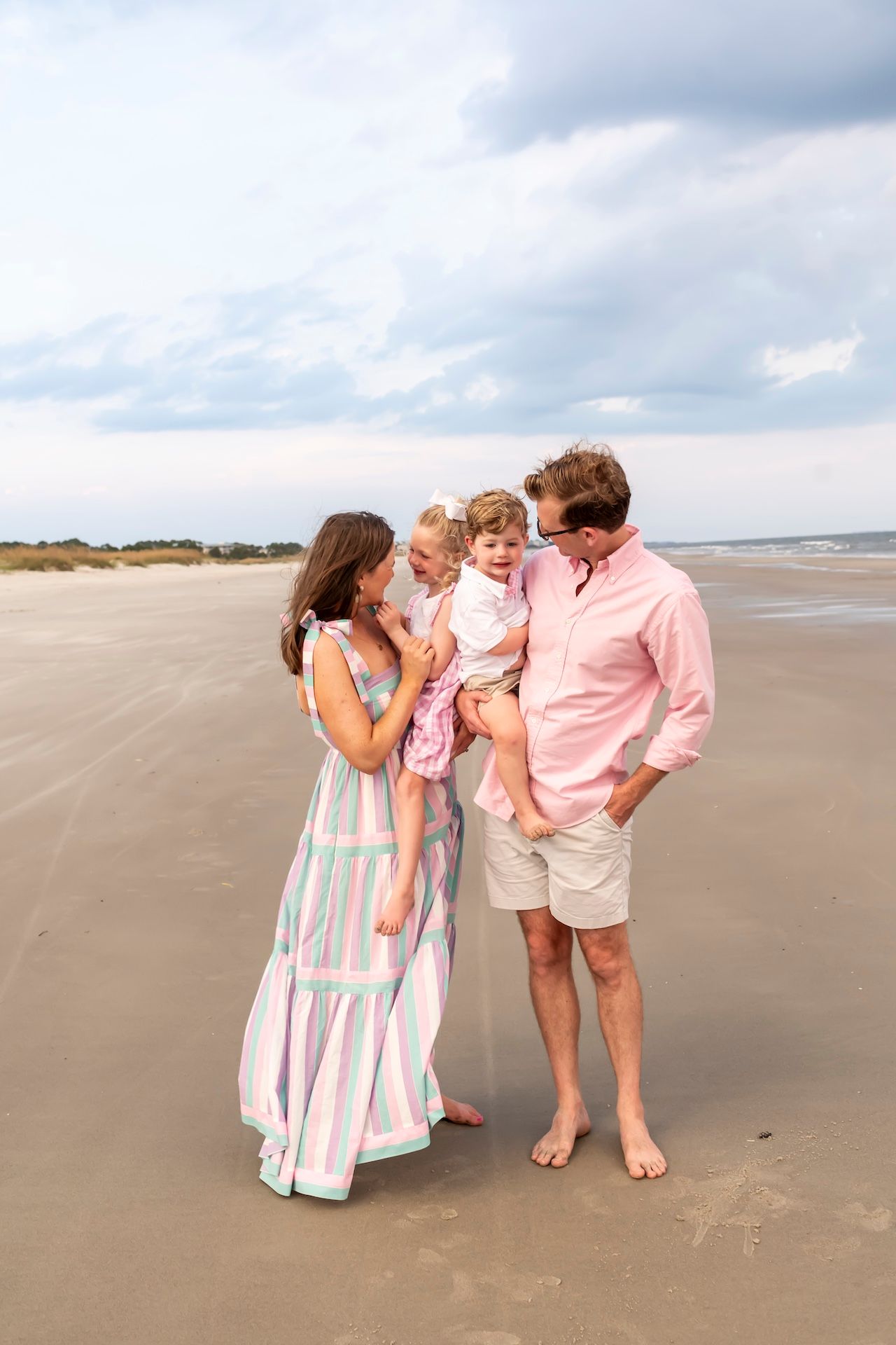 Family in coordinating pastel outfits sharing a tender moment together on a cloudy beach.