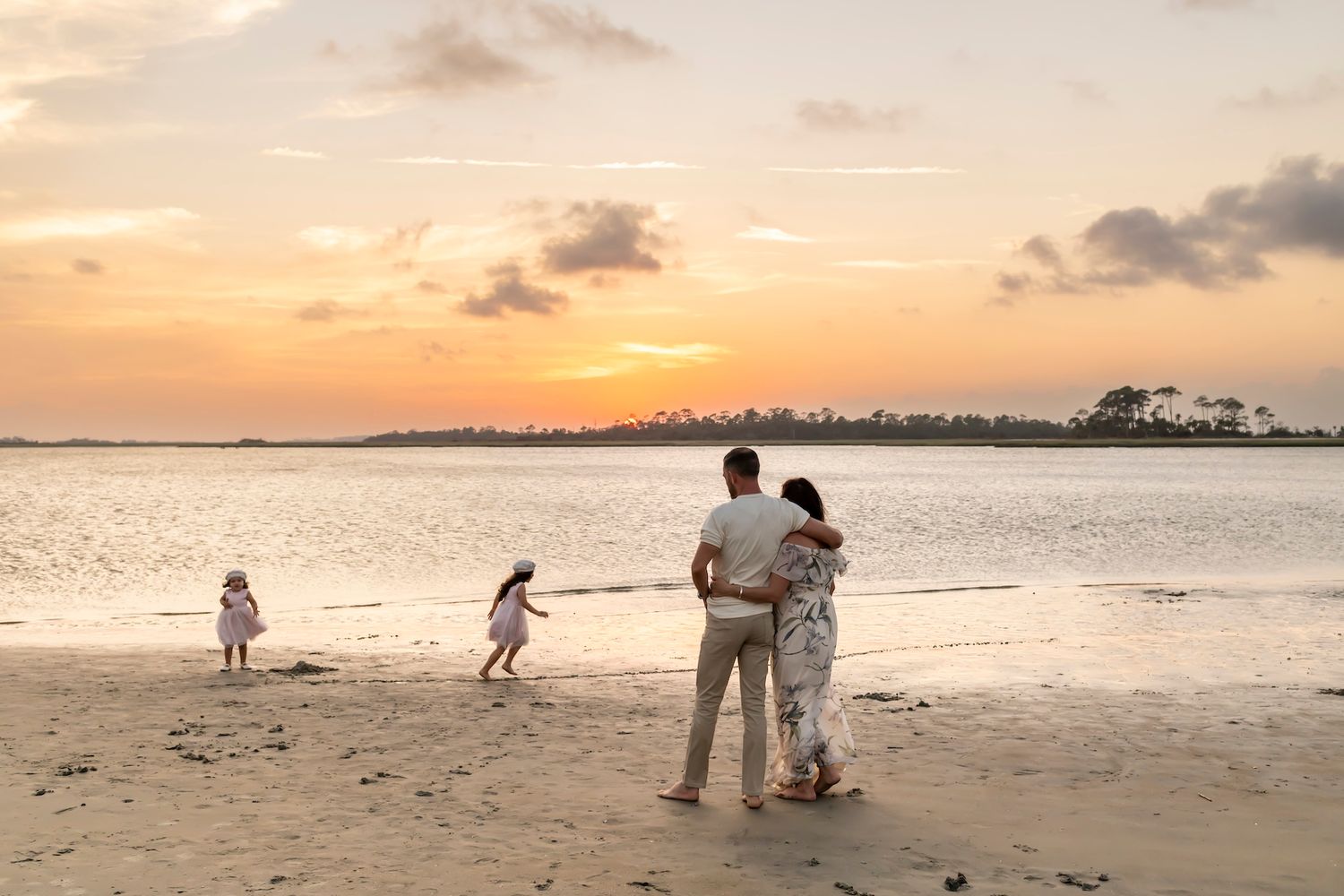 Group of people enjoying a scenic sunset on a tropical beach shoreline with gentle waves and warm lighting.