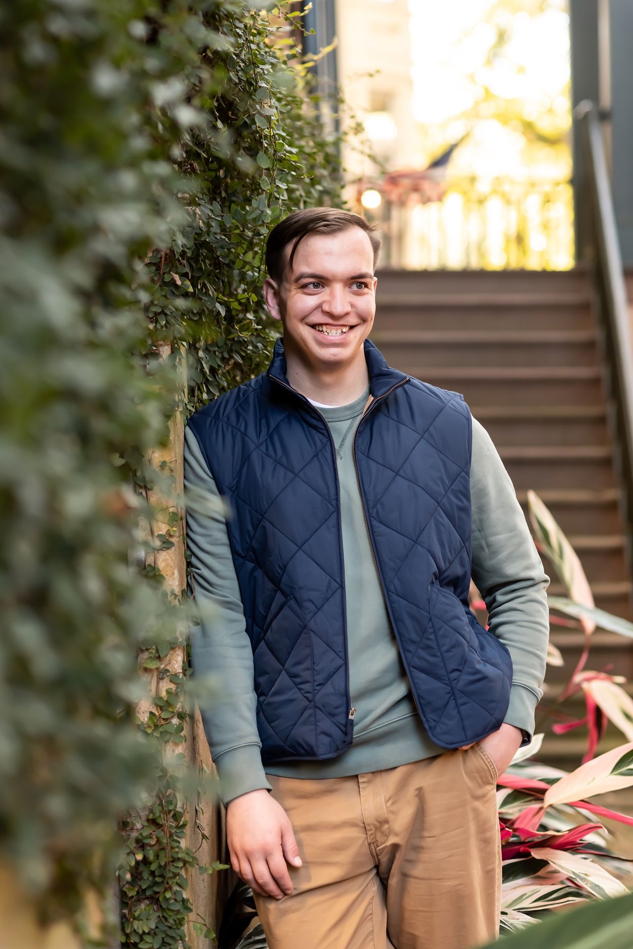 A person in a navy quilted vest and gray sweater sits on stone steps during autumn.