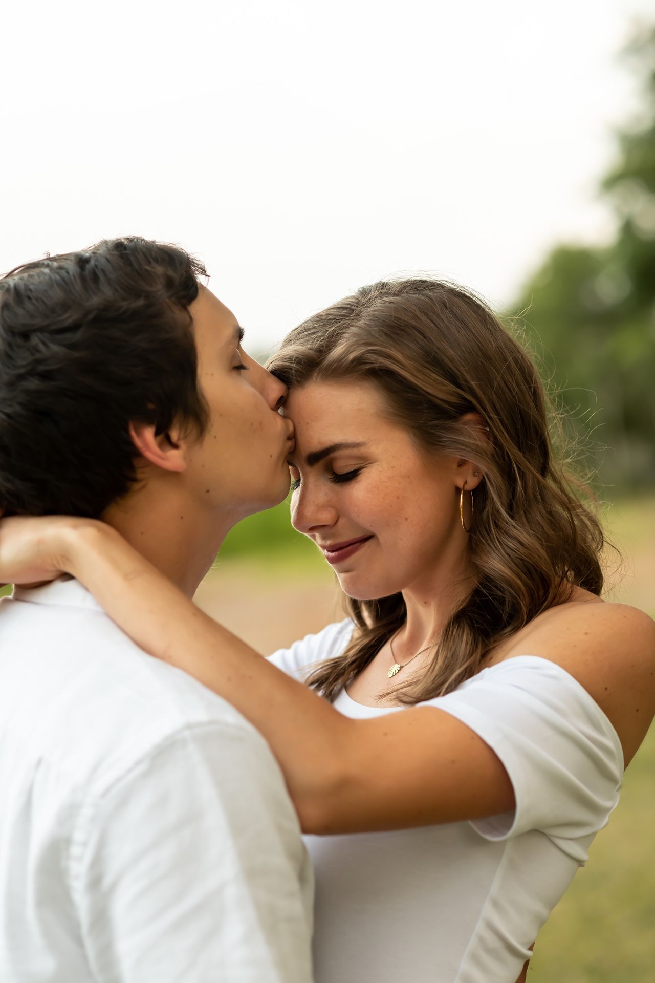 A tender moment between a couple as they embrace and share affectionate gestures outdoors.