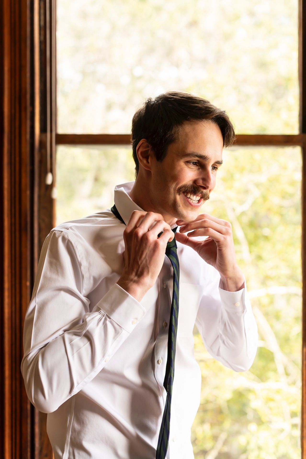 A split image shows sequences of someone adjusting their black necktie while wearing a white dress shirt near a window.