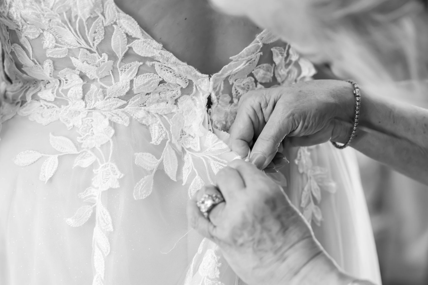 Close-up detail shot of hands buttoning an intricate lace wedding dress.