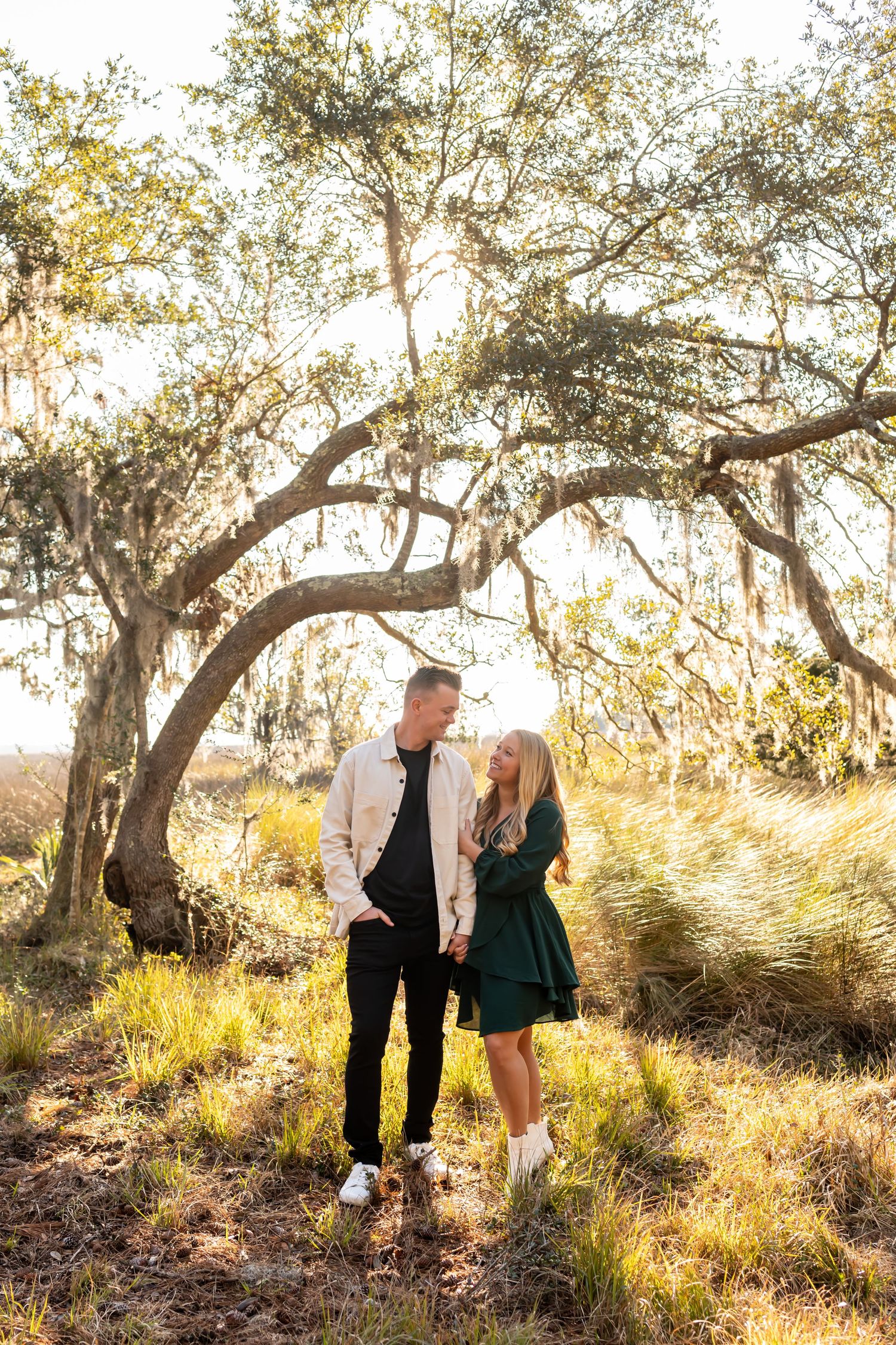 A couple poses together near trees in golden sunlight during an outdoor photoshoot.