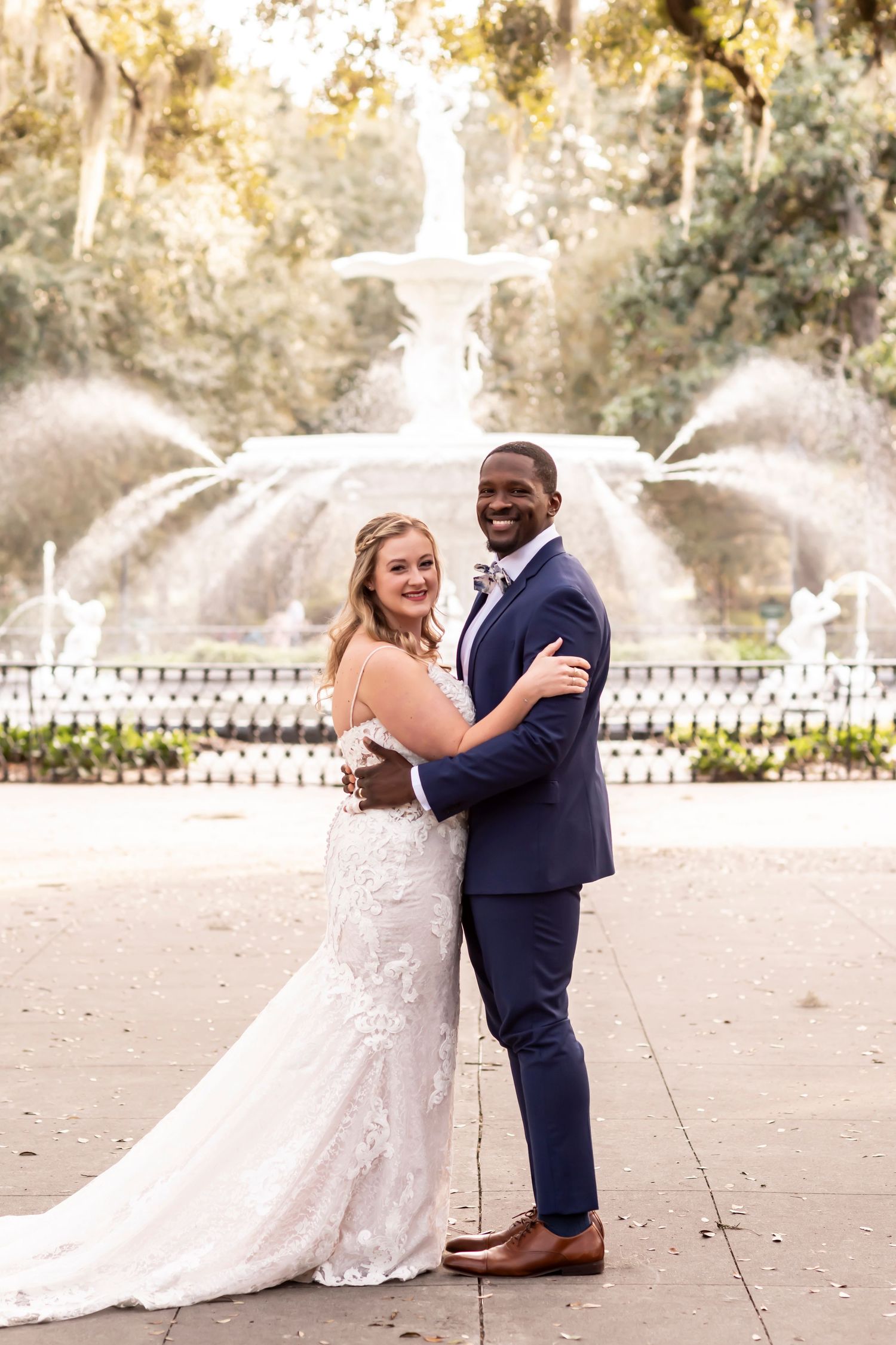 Happy couple sharing joyful dance moments at wedding celebration on sunny day with white picket fence in background.
