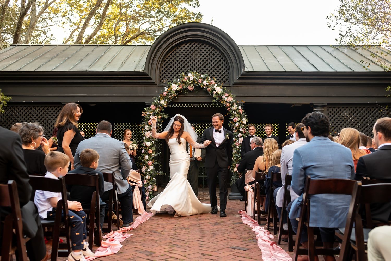A wedding ceremony setup with white chairs arranged in rows along a decorated outdoor aisle with flower petals.