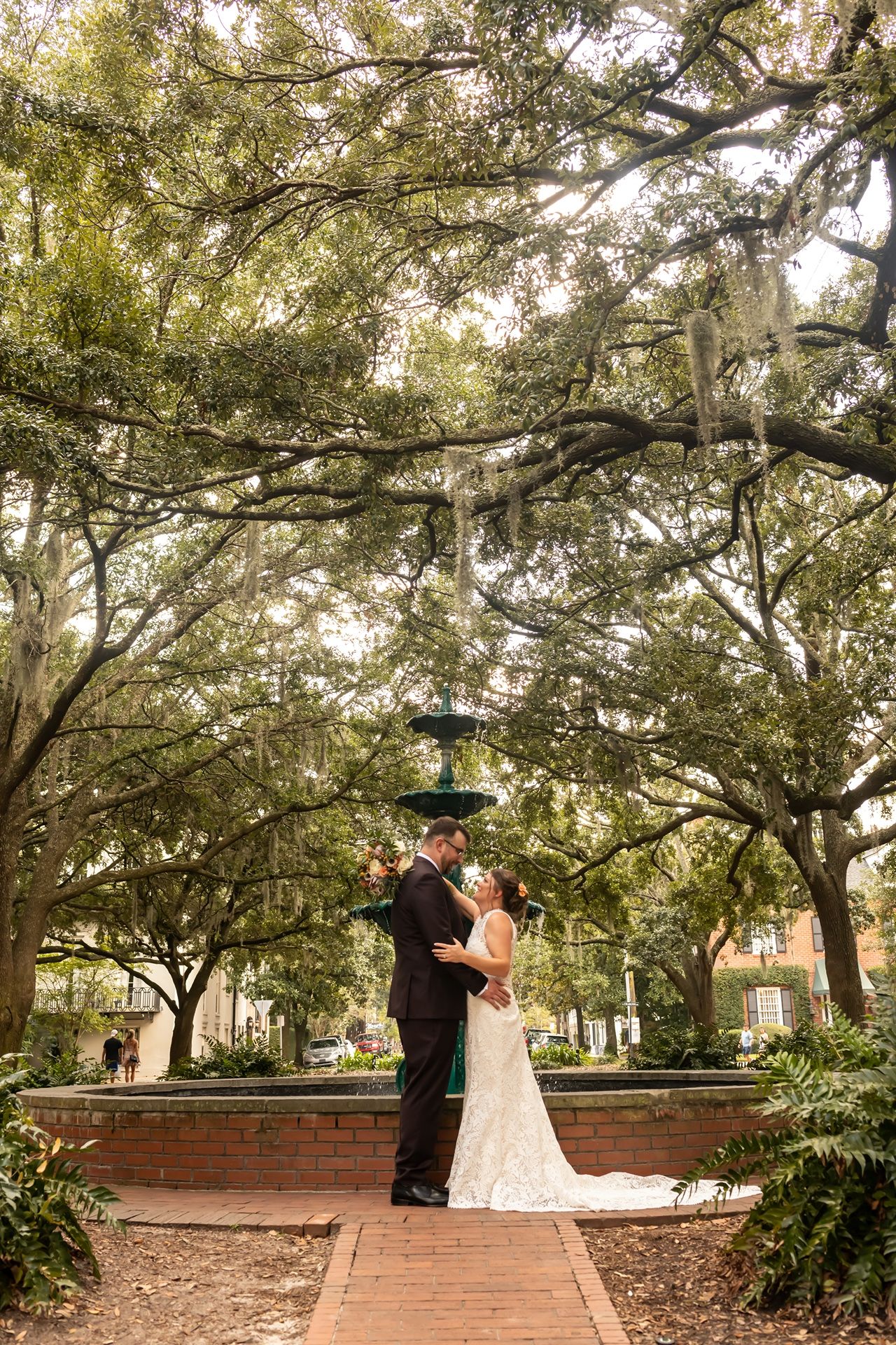 Romantic couple shares an intimate moment under moss-draped oak trees in a scenic garden pathway.
