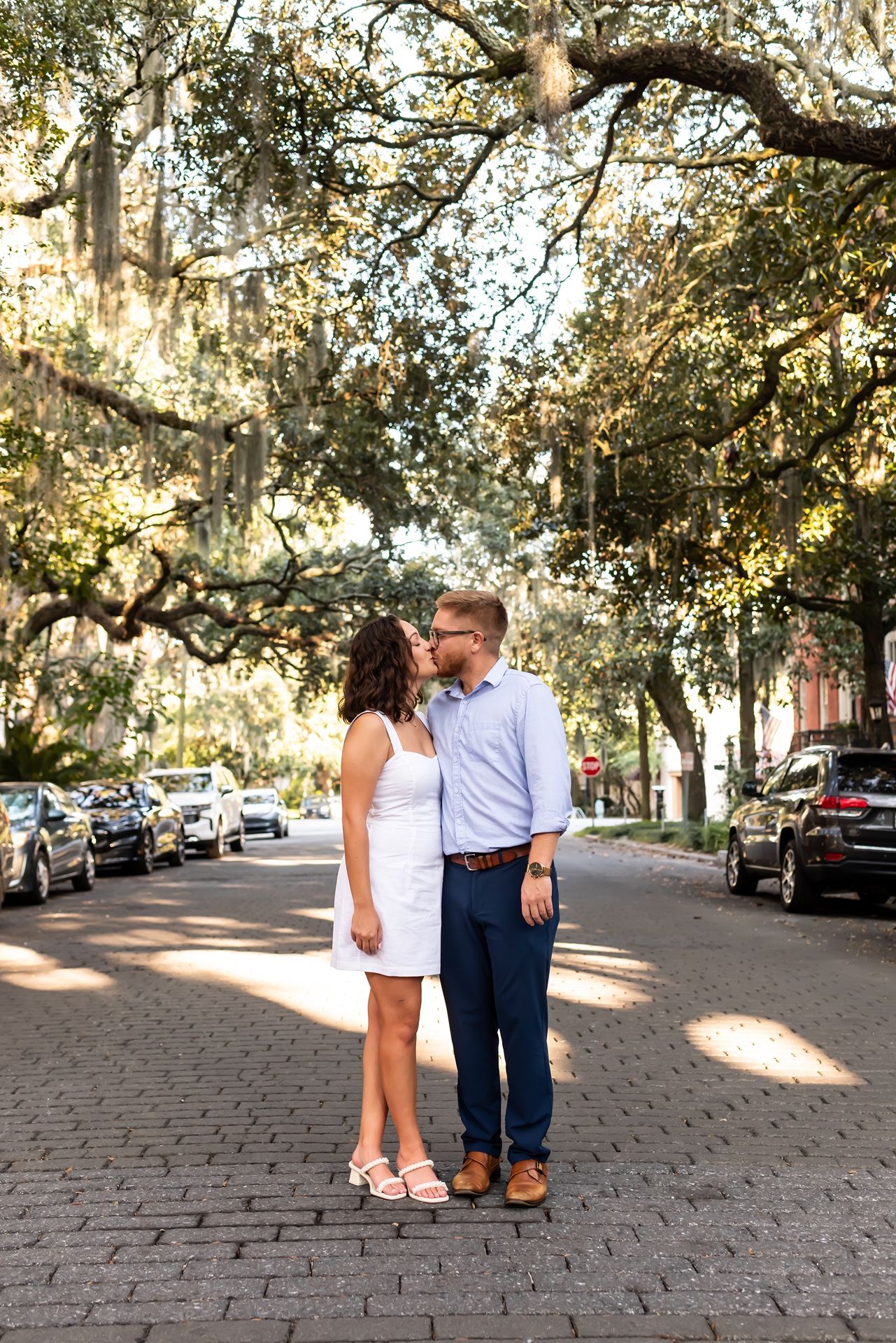 A romantic couple shares a tender moment walking along a charming tree-lined cobblestone street.