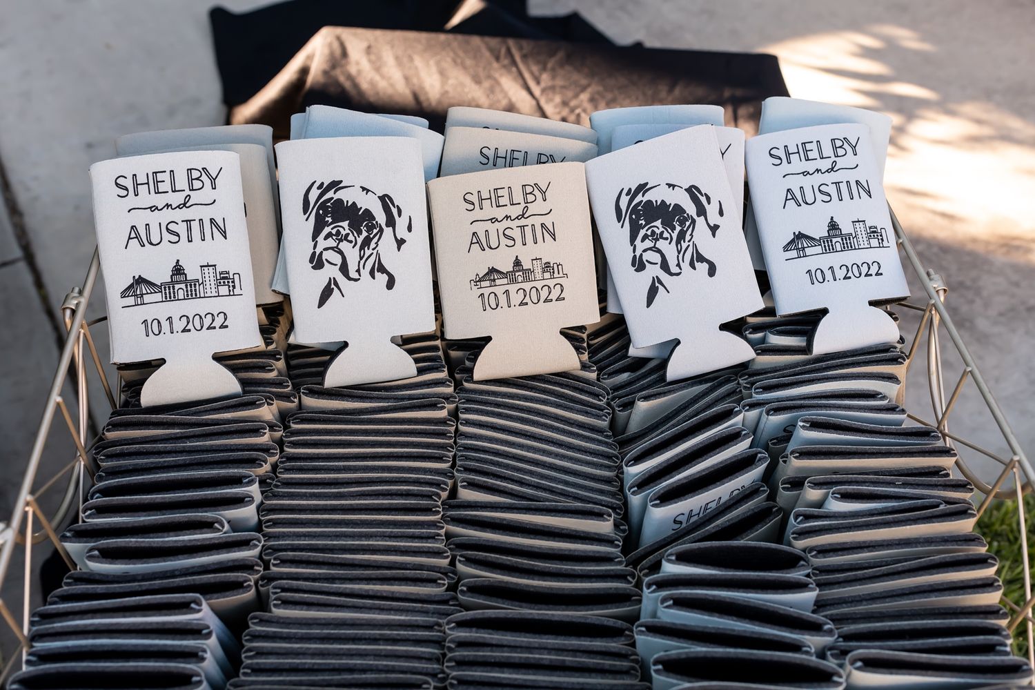 Wedding koozies with black and white stripes and buffalo designs stacked neatly in rows at outdoor event.