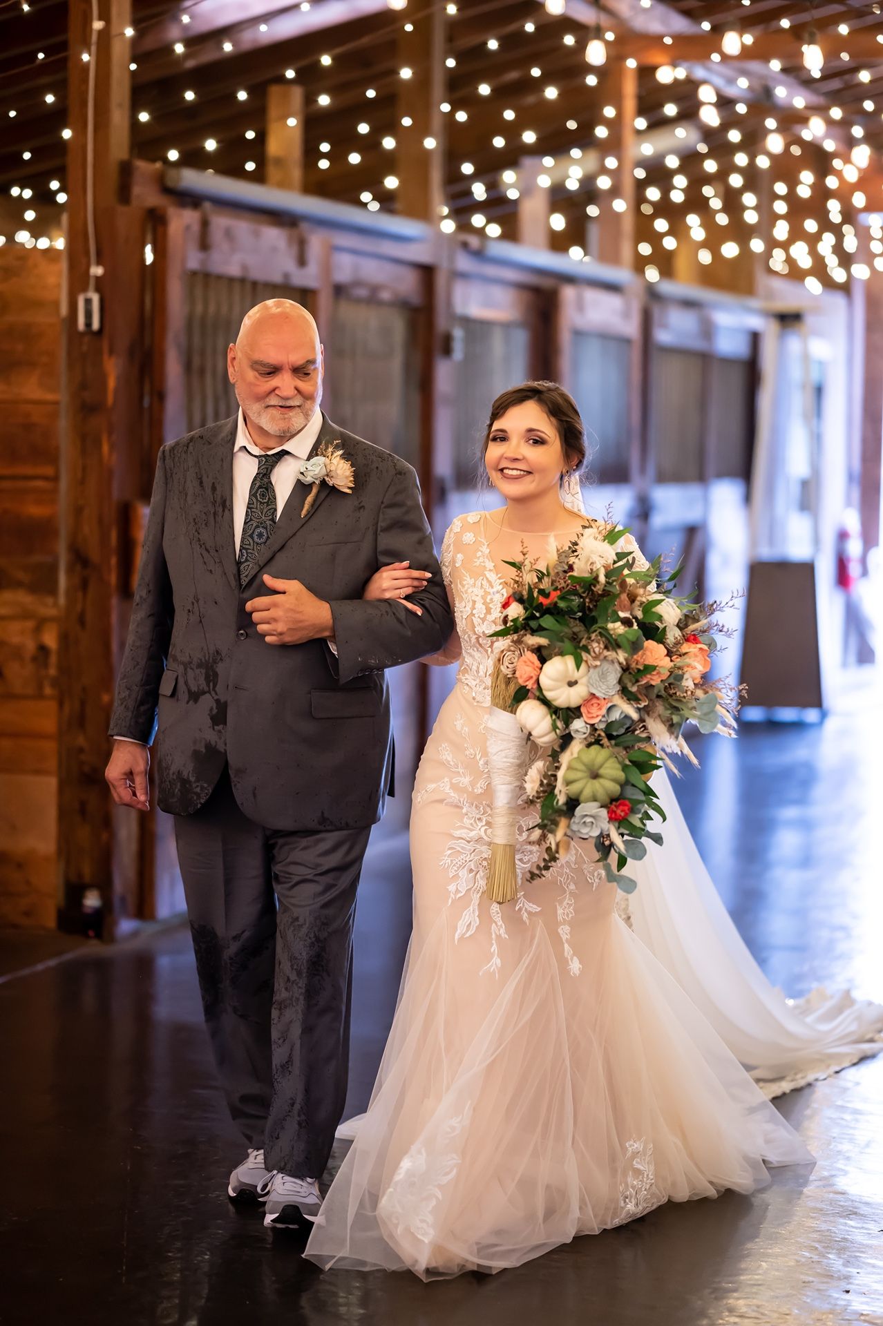 A formal wedding ceremony in a rustic barn venue decorated with twinkling string lights overhead.