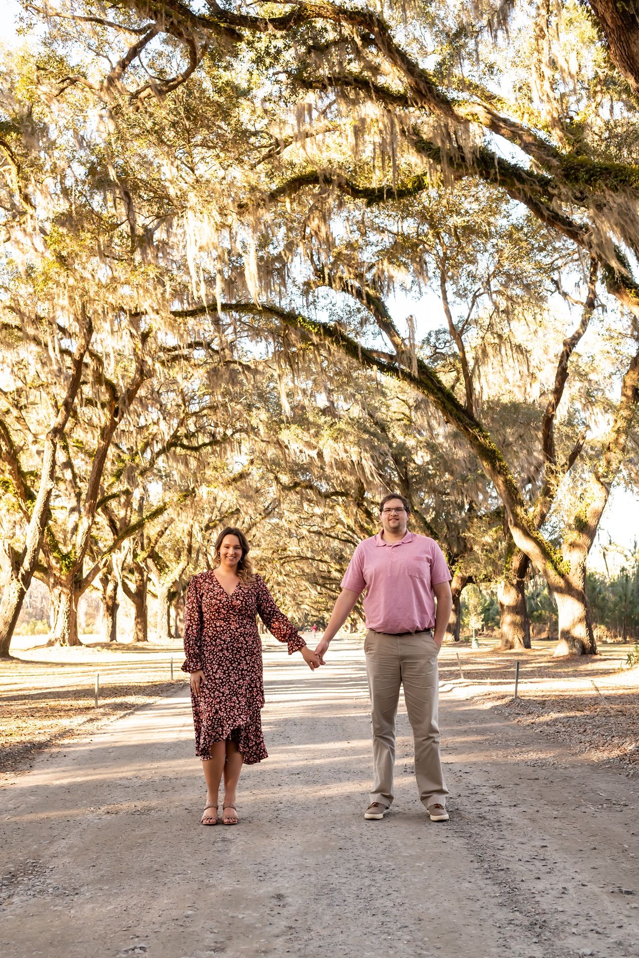 A couple walks hand in hand down a scenic path lined with Spanish moss-covered oak trees.