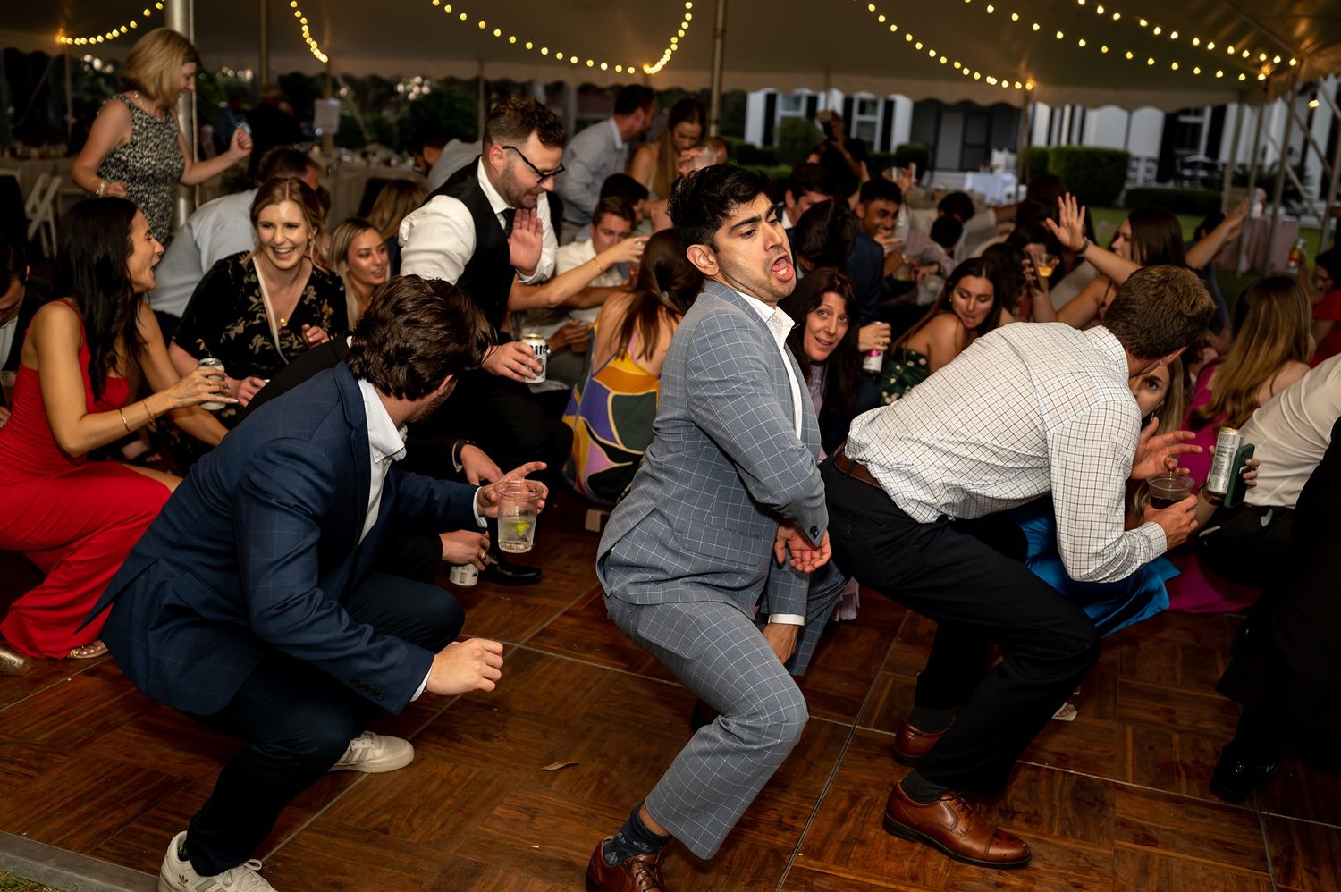 Party guests enjoying lively dancing and entertainment at a dimly lit indoor reception venue.