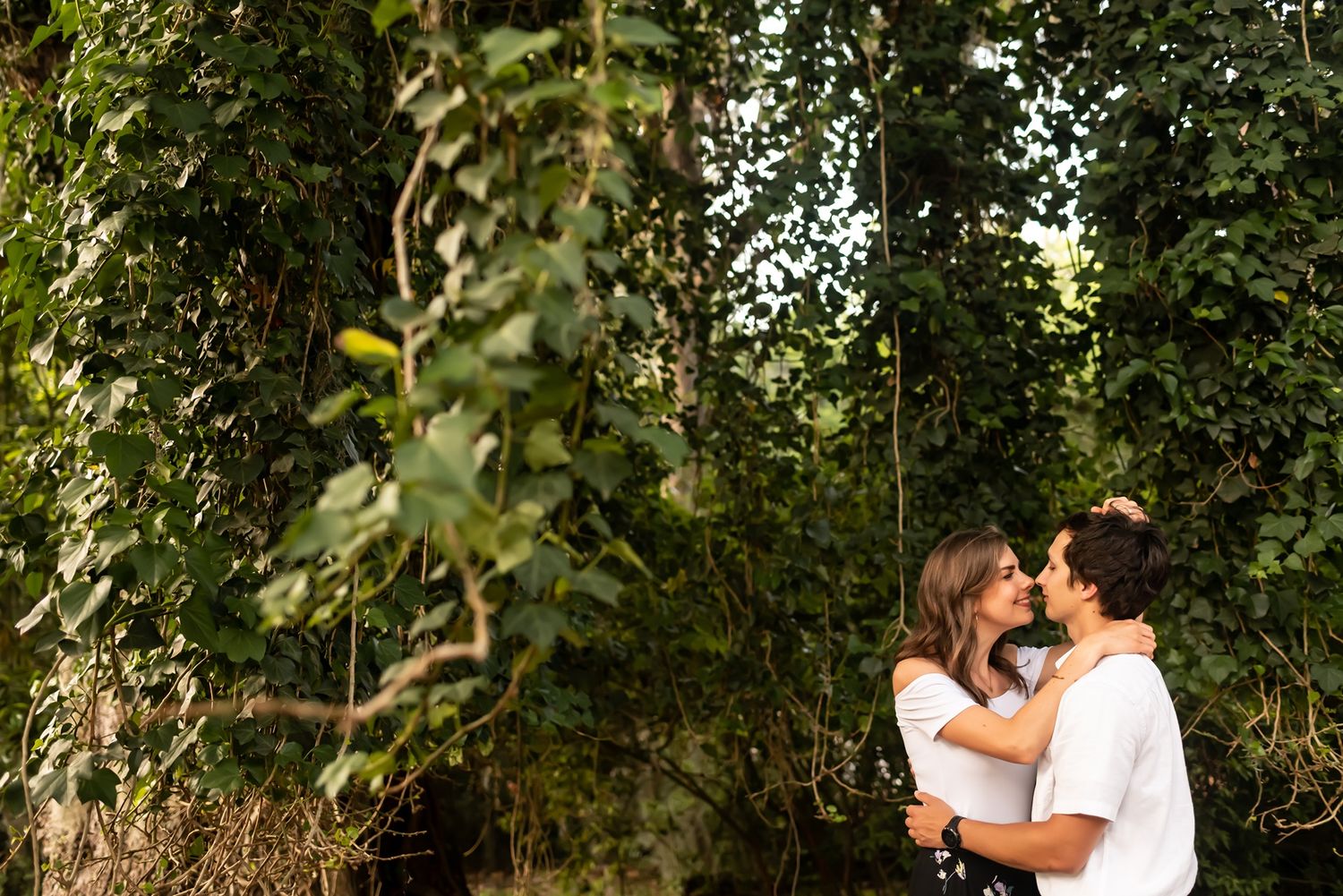 A couple embraces intimately among lush green trees in a romantic outdoor photoshoot.