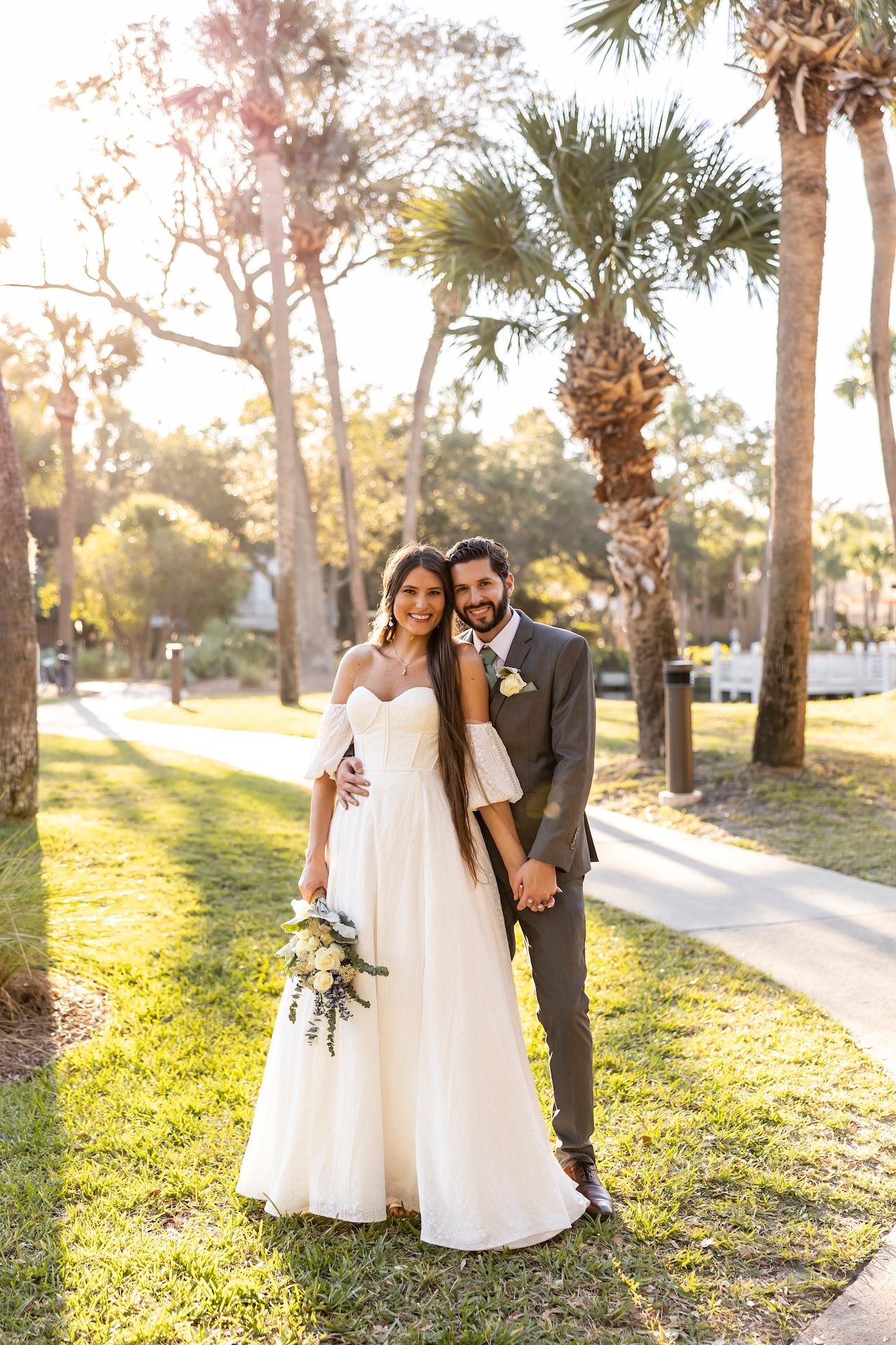 A romantic wedding couple poses in a sun-drenched park with palm trees and golden sunlight creating a dreamy atmosphere.