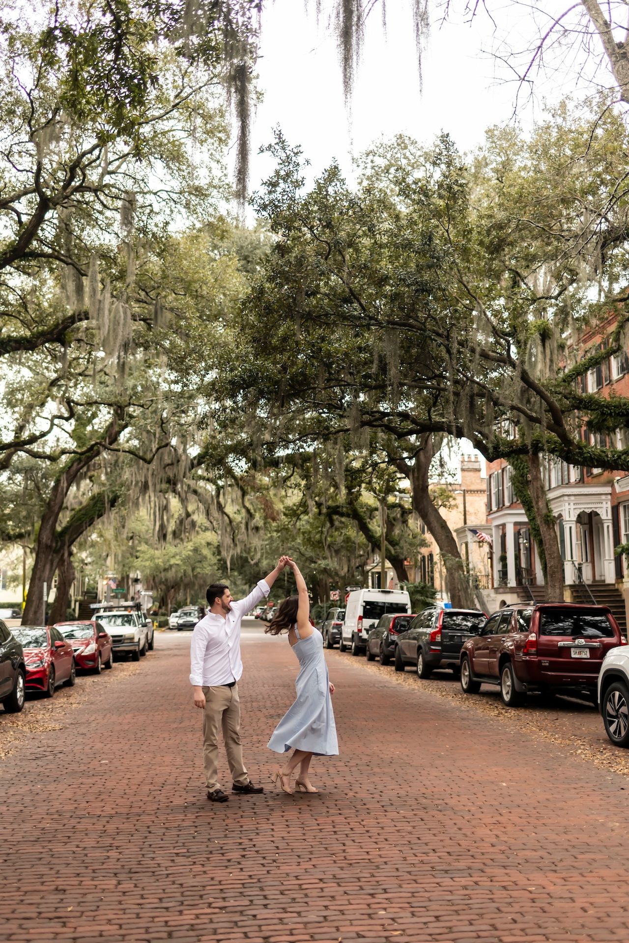 A couple dances together on a historic brick-lined street with Spanish moss draped oak trees in Savannah, Georgia.