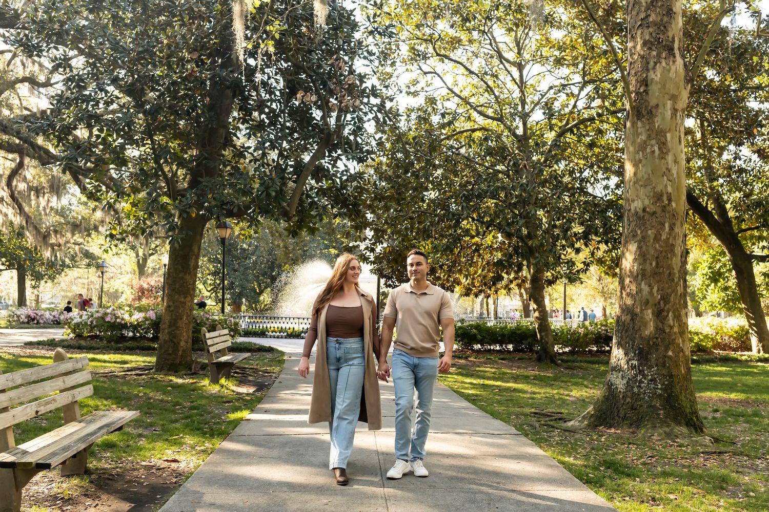 Two people walking together on a peaceful tree-lined path in a sunlit park on a warm autumn day.