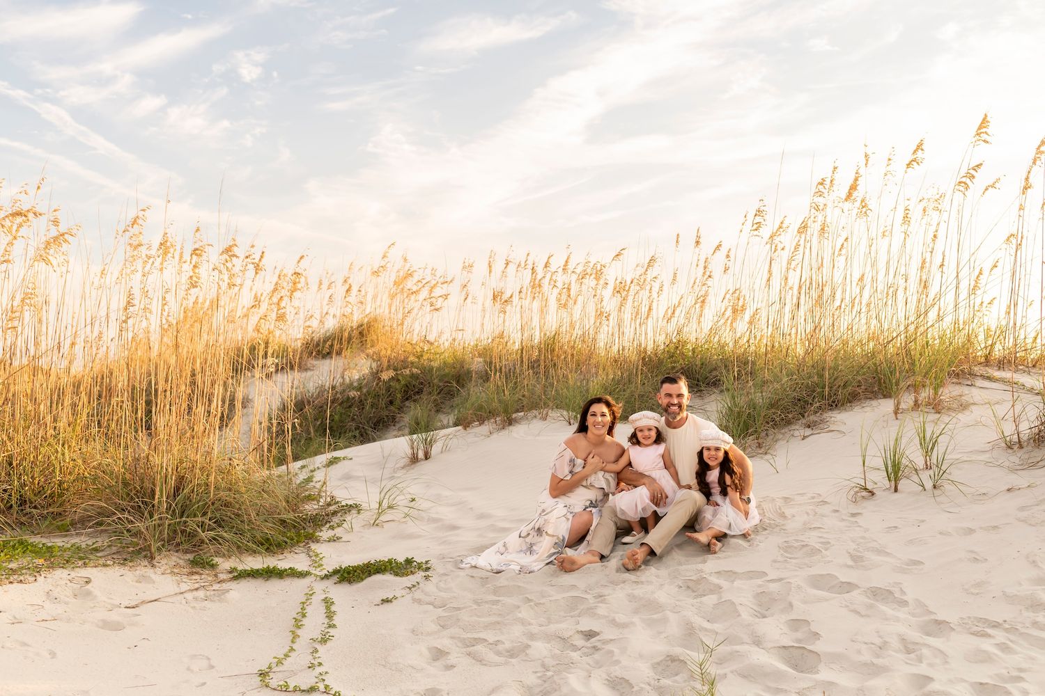 A joyful beach scene with people sitting in golden sea oats and sand dunes at sunset.