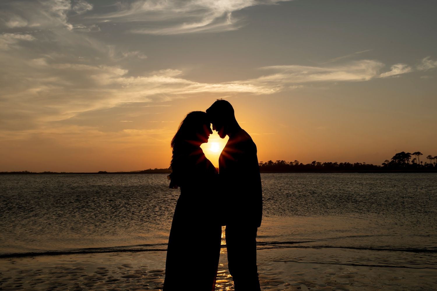 Silhouette of two people sharing an intimate moment against a dramatic sunset sky over water.