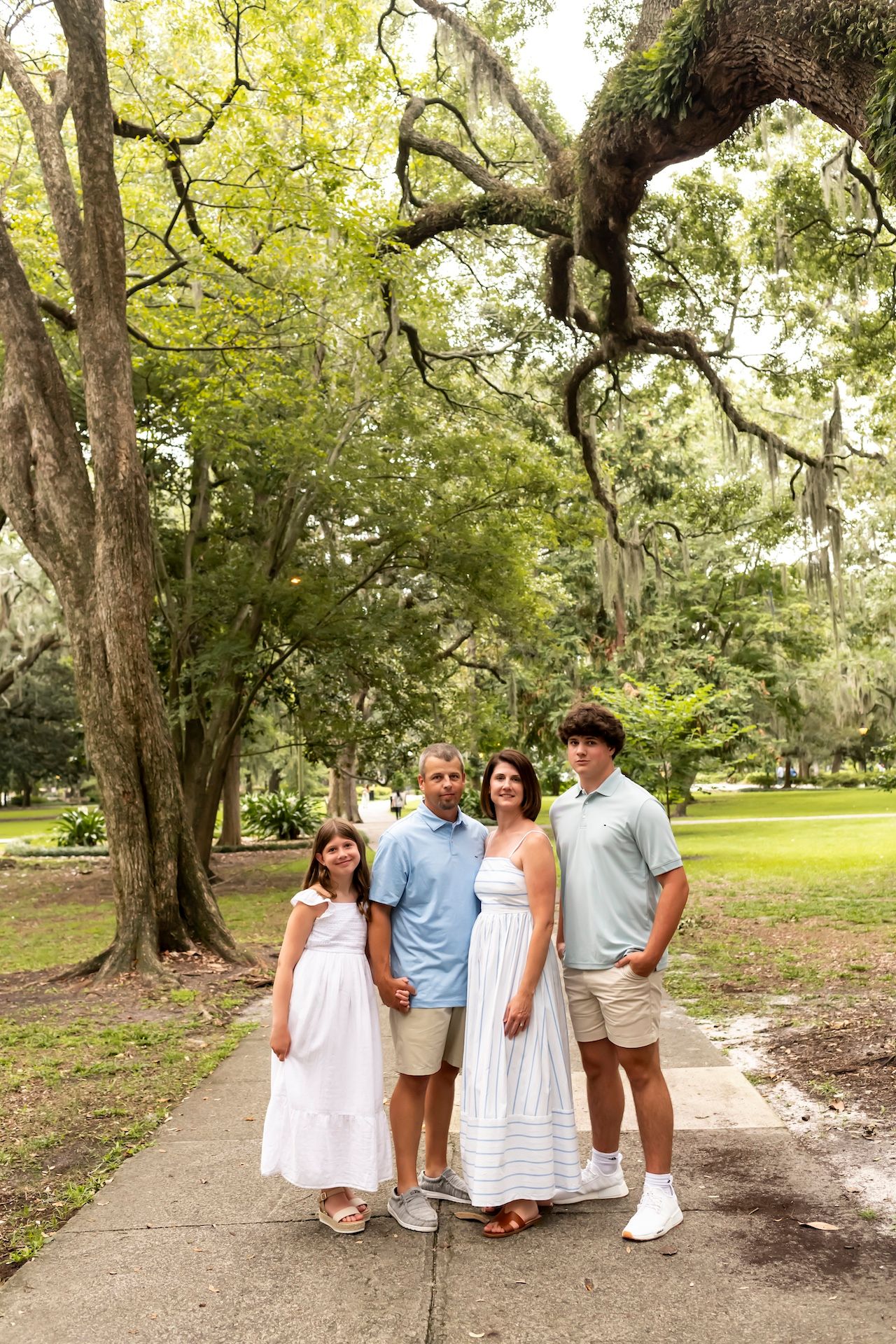 Family of four poses together on path beneath large oak trees draped in Spanish moss.