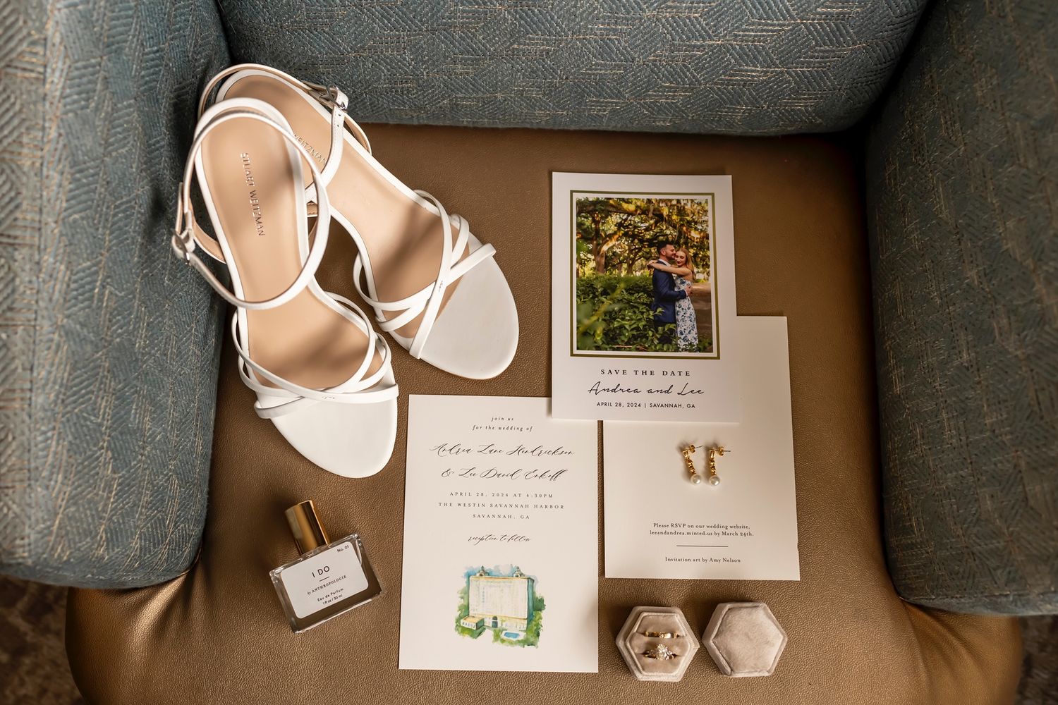 Wedding details flatlay with white sandals, invitation cards and decor arranged on gray couch cushion.