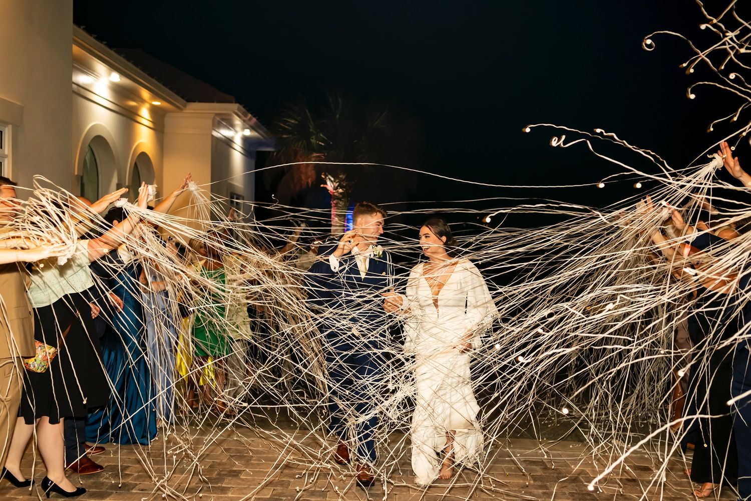 Long strands of white string create an intricate web-like pattern connecting performers in a dimly lit performance space.