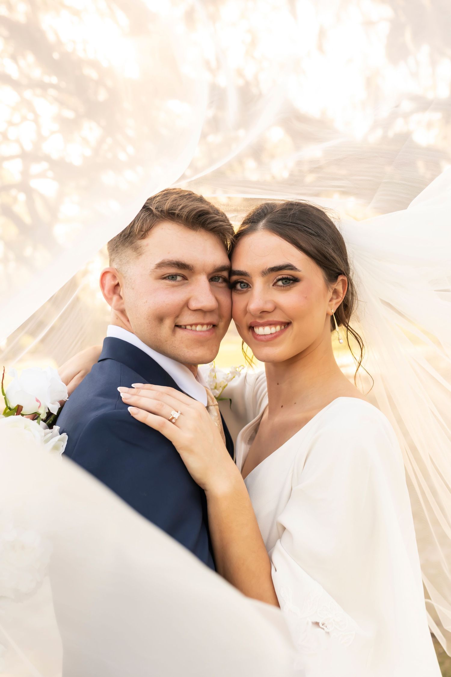 A beaming couple embraces on their wedding day, with a flowing veil and beautiful soft lighting creating a romantic atmosphere.