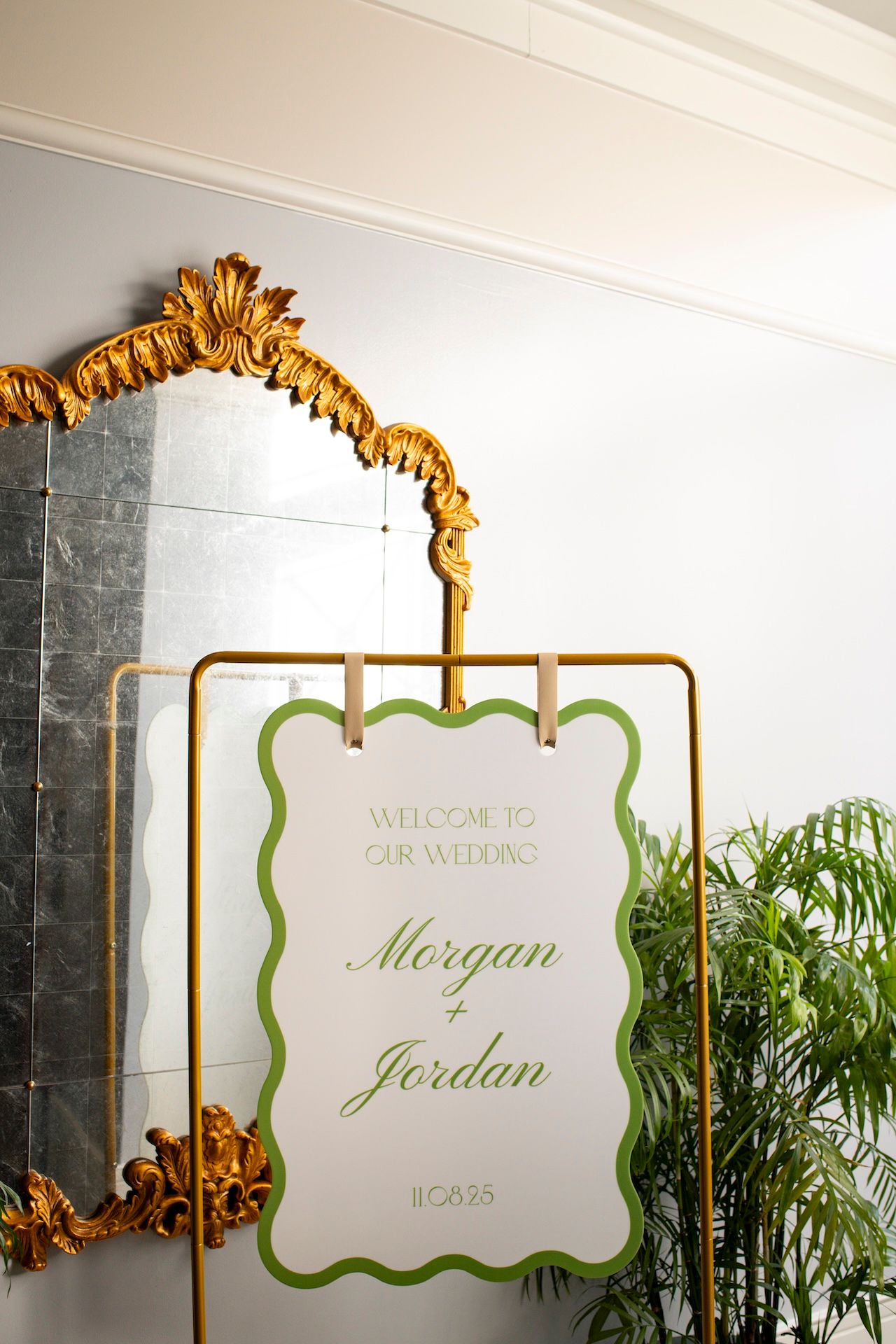 Elegant gold-framed welcome sign with green accents and calligraphy displayed at a wedding reception entrance.