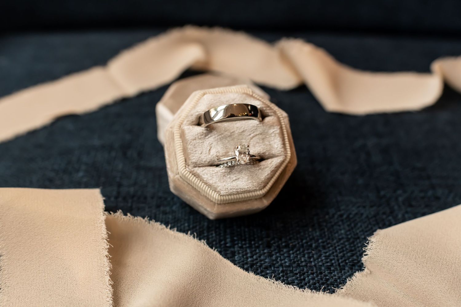 Wedding rings displayed on dark fabric with artistic lighting and shallow depth of field.