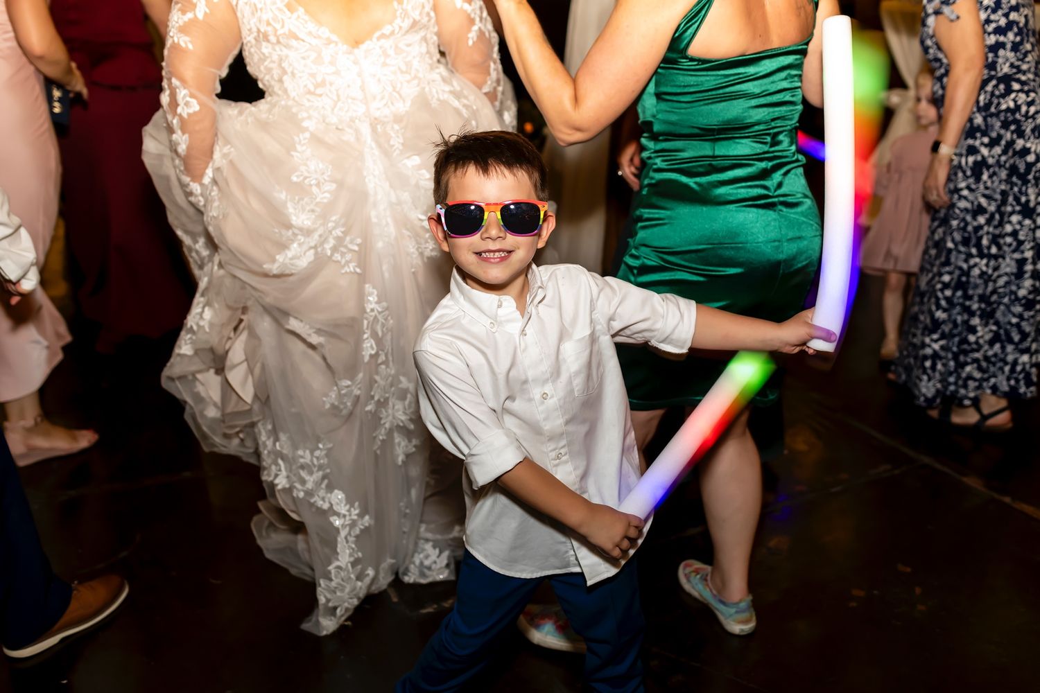 Young party guest in sunglasses and white shirt dances with a glow stick on the dance floor at a wedding reception.